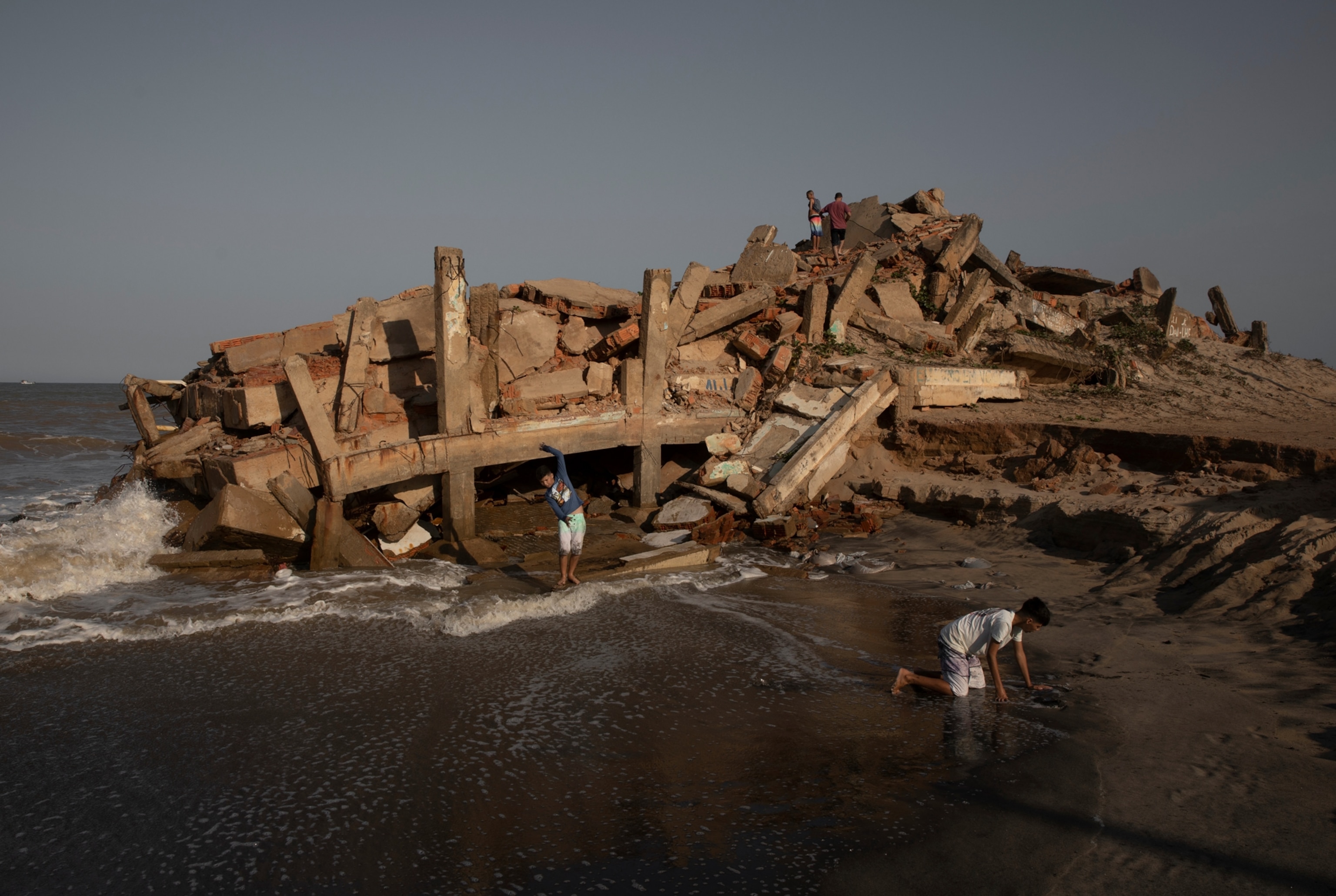 children play on the ruins of a building as the ocean waves lap on the edge of the rubble