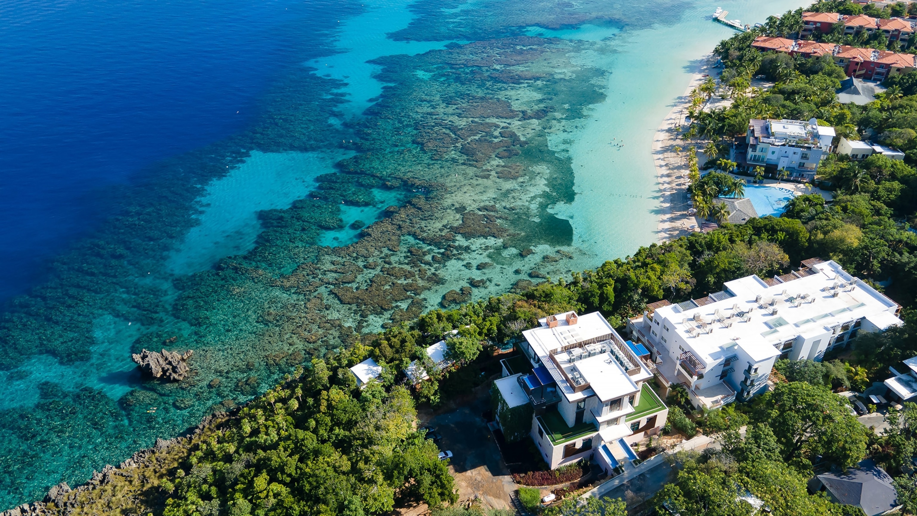 An aerial view of the Kimpton Grand Roatán Resort & Spa situated near the coastline with the The Mesoamerican Reef just offshore.