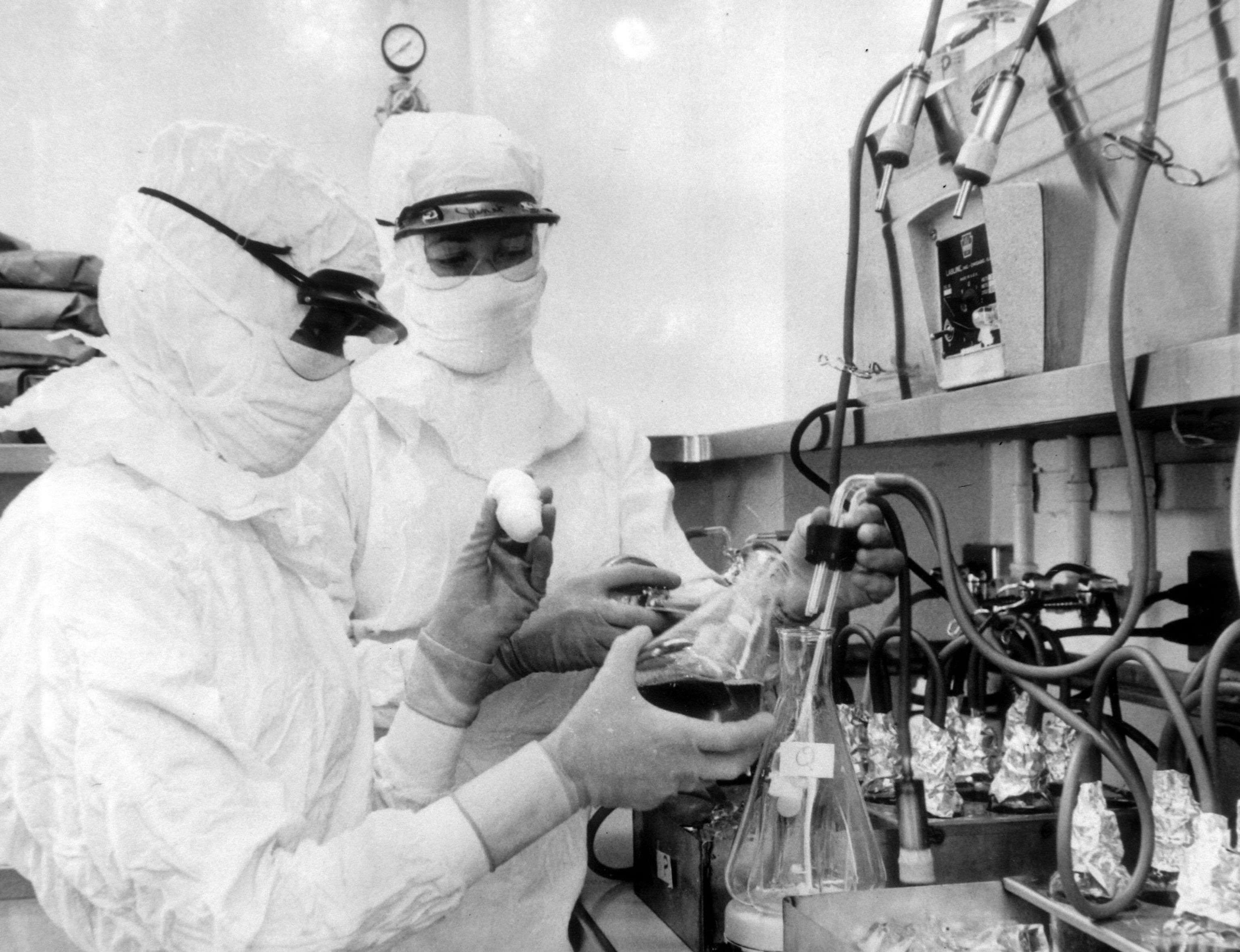 Black and white photograph of two men in hazmat suits working with laboratory equipment