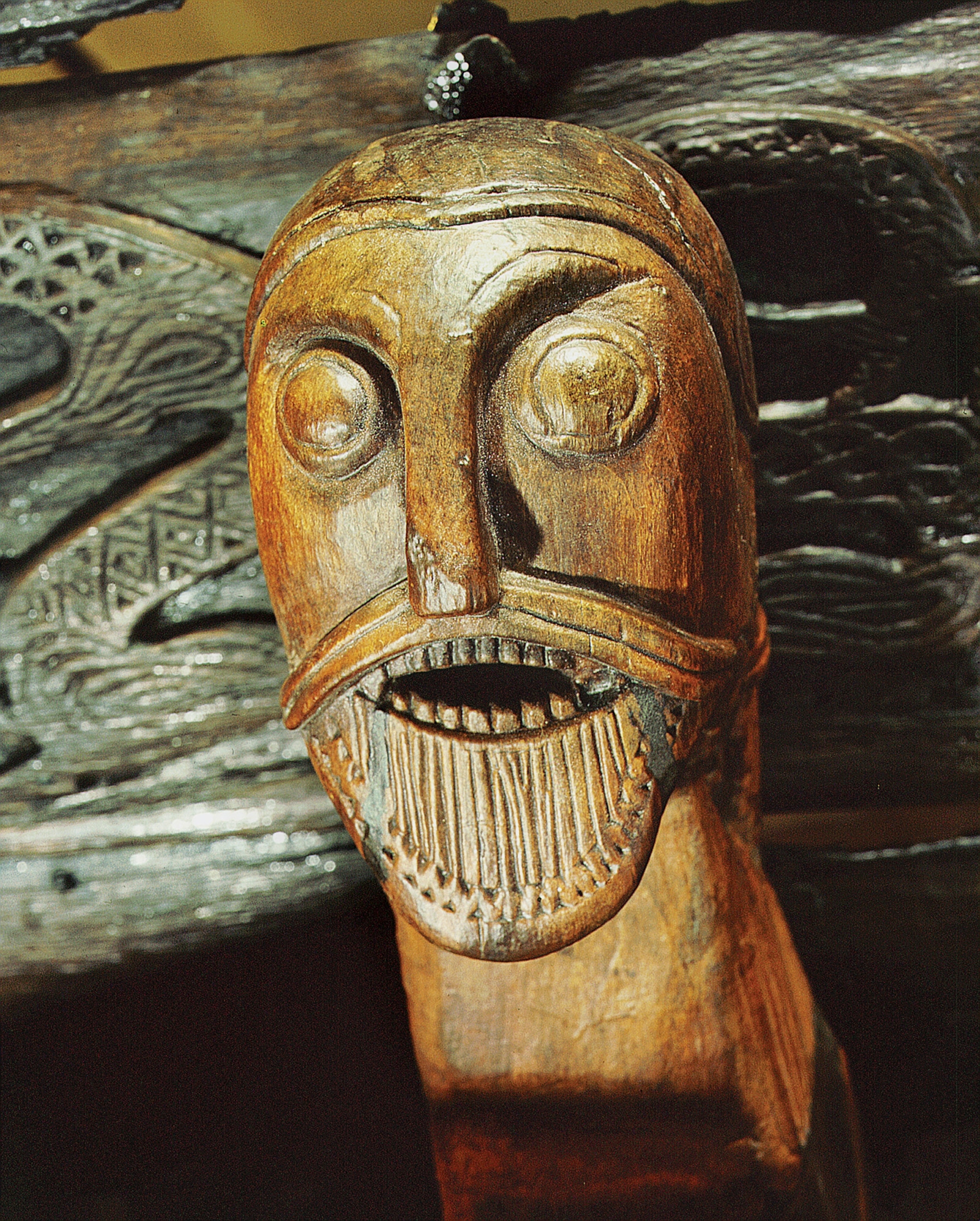 A fierce face bares its teeth on the side of the Oseberg cart.