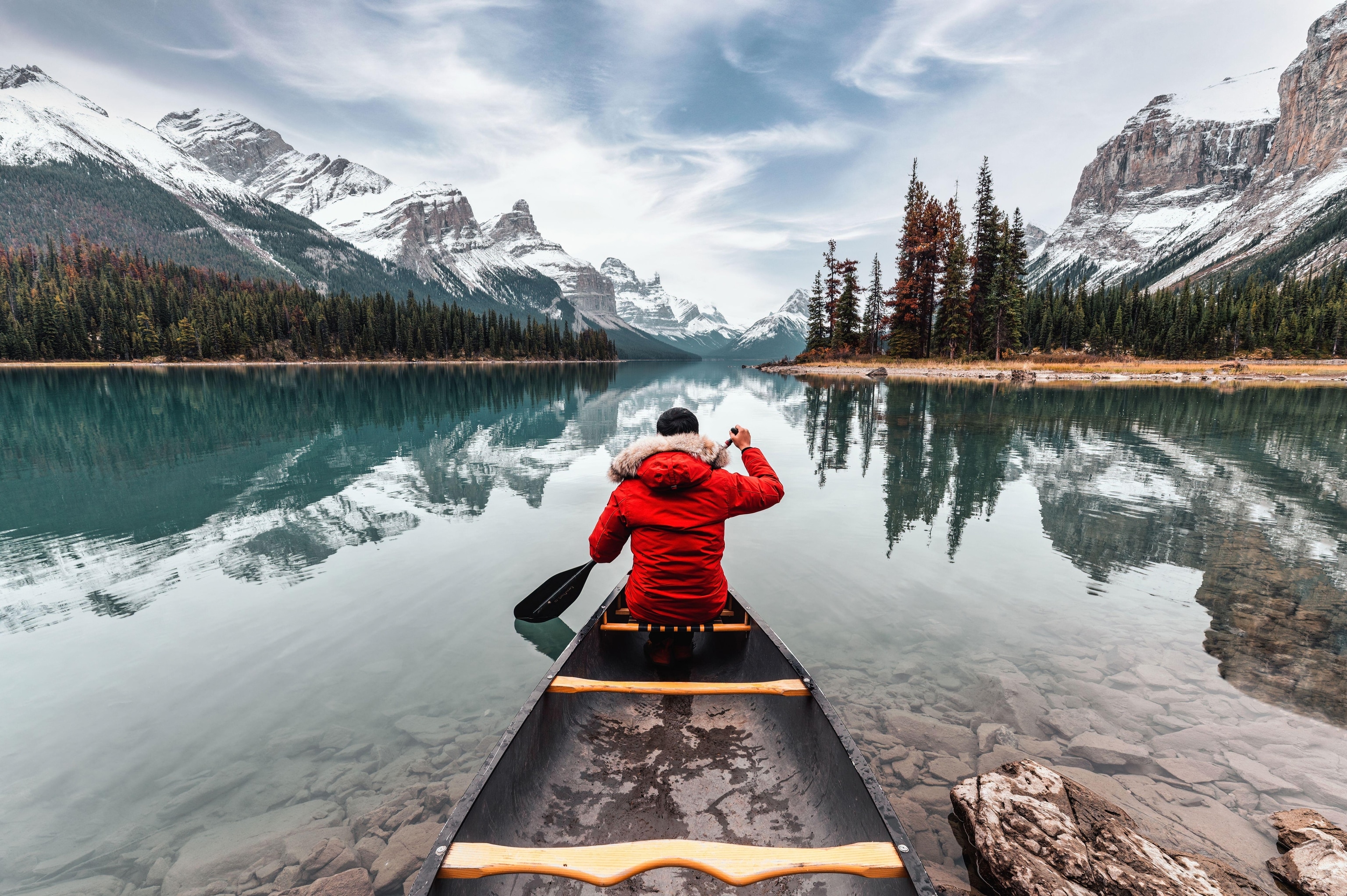 Male traveler in winter coat canoeing on lake with mountains