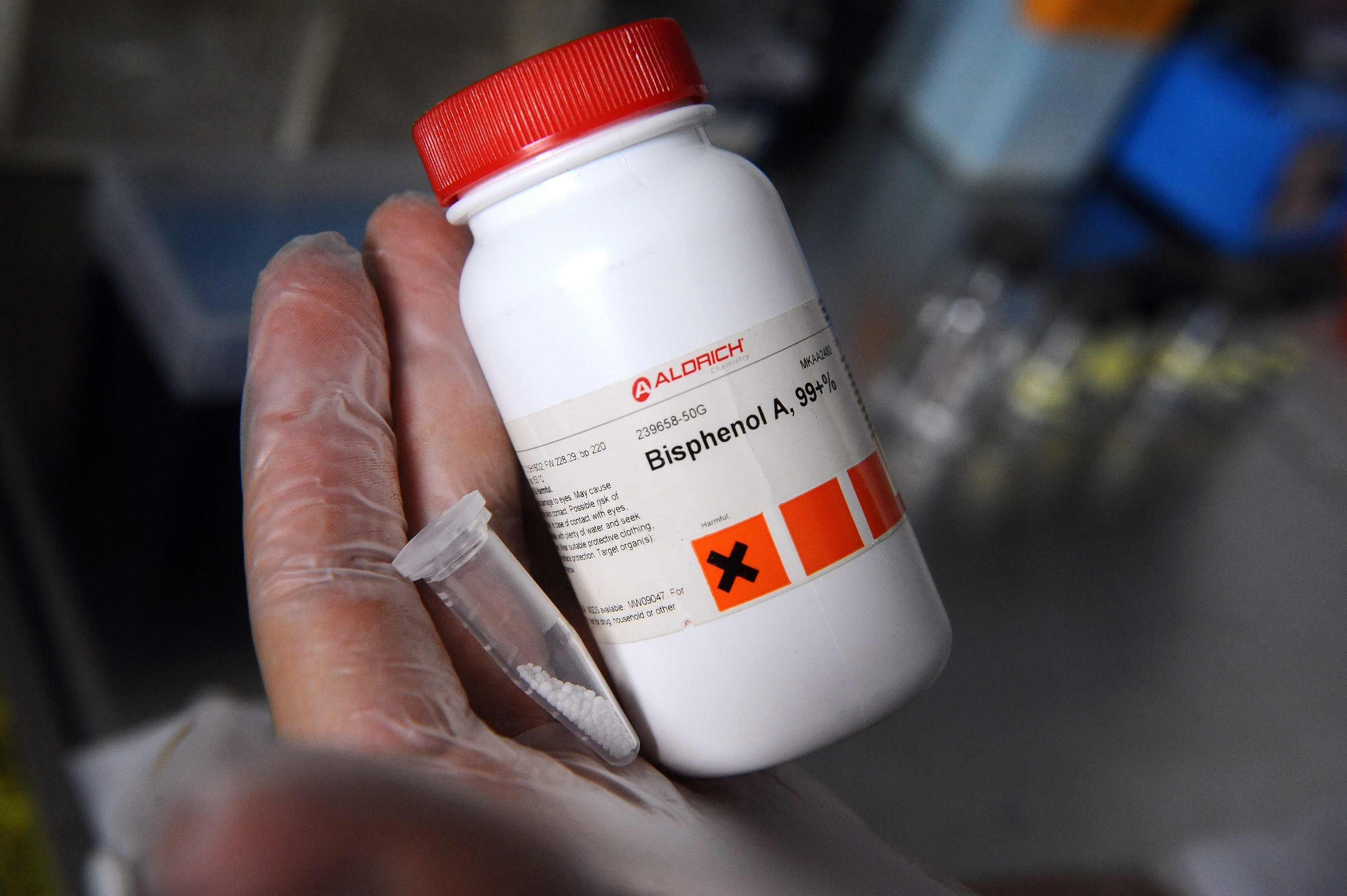 a gloved hand holding a plastic bottle and a vial holding small white plastic beads