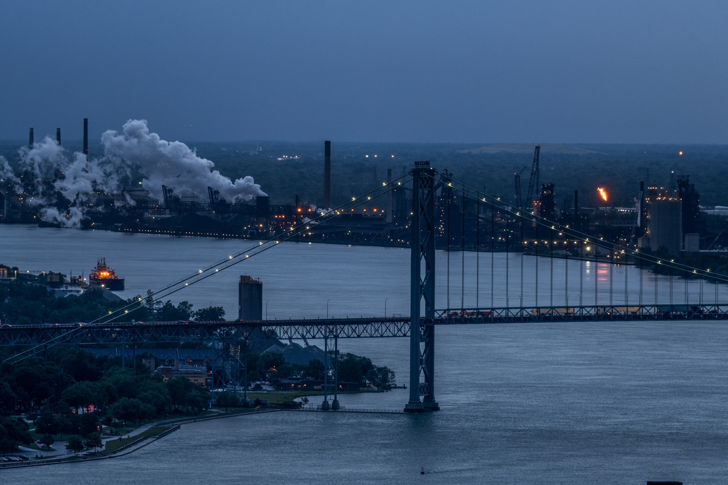 city along river with bridge over it and industrial smokes on the background at dusk.