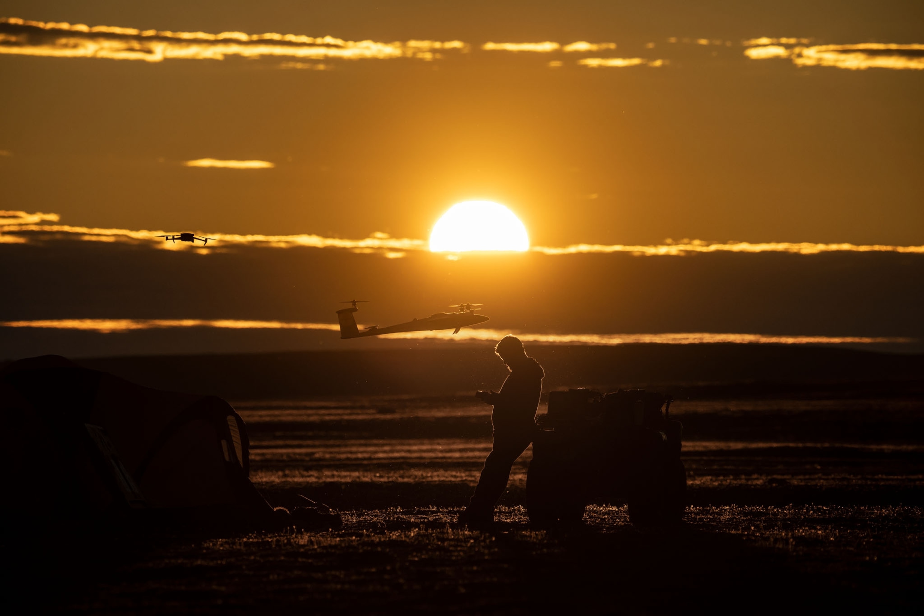 Man and drone above him against sunset.