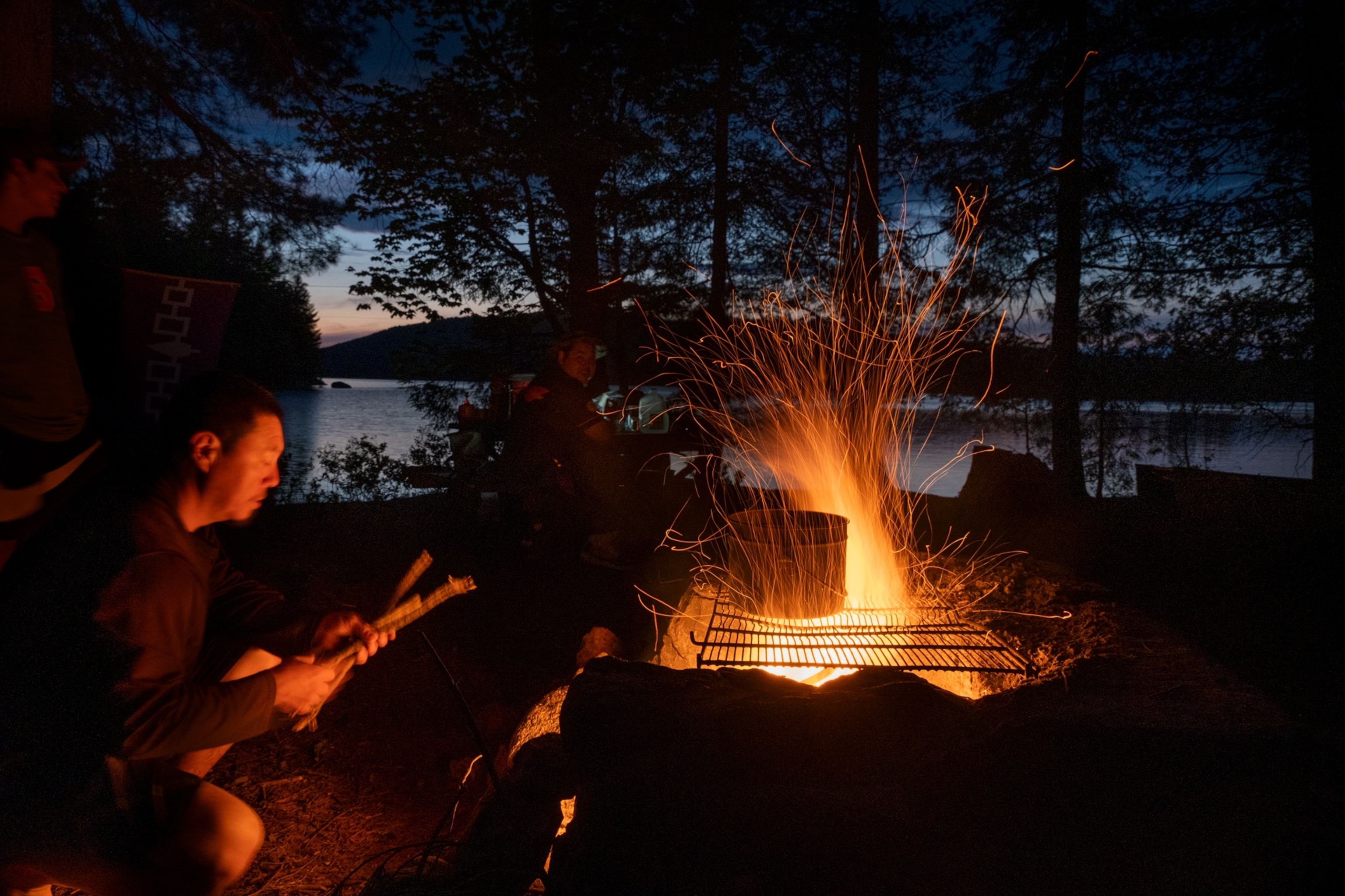 An individual tends to a fire during sunset by a lake