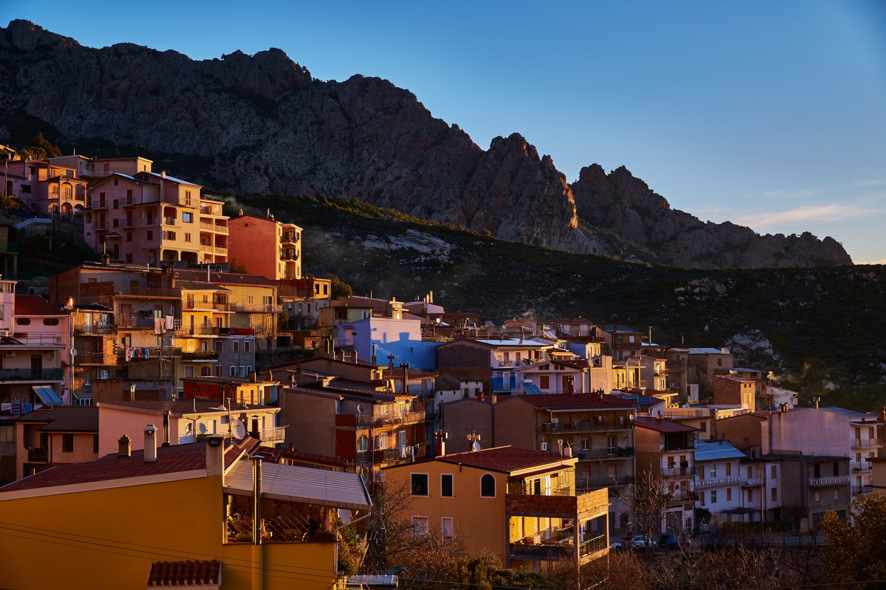 Sunlight shines on houses within a mountain valley of Sardinia.