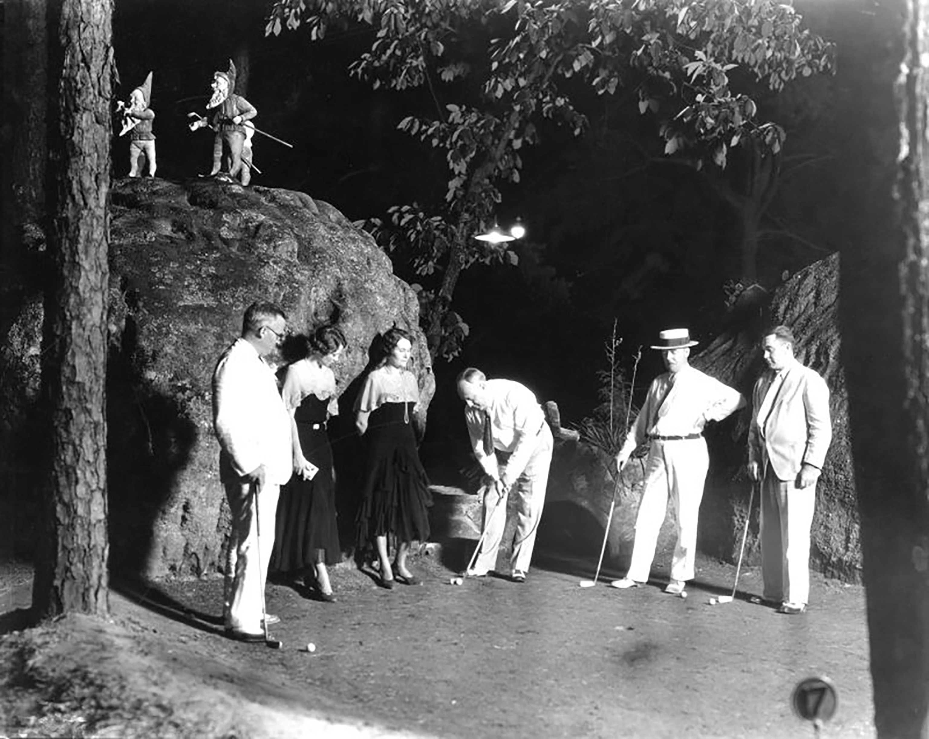 One man putts as 2 women and 3 men watch.