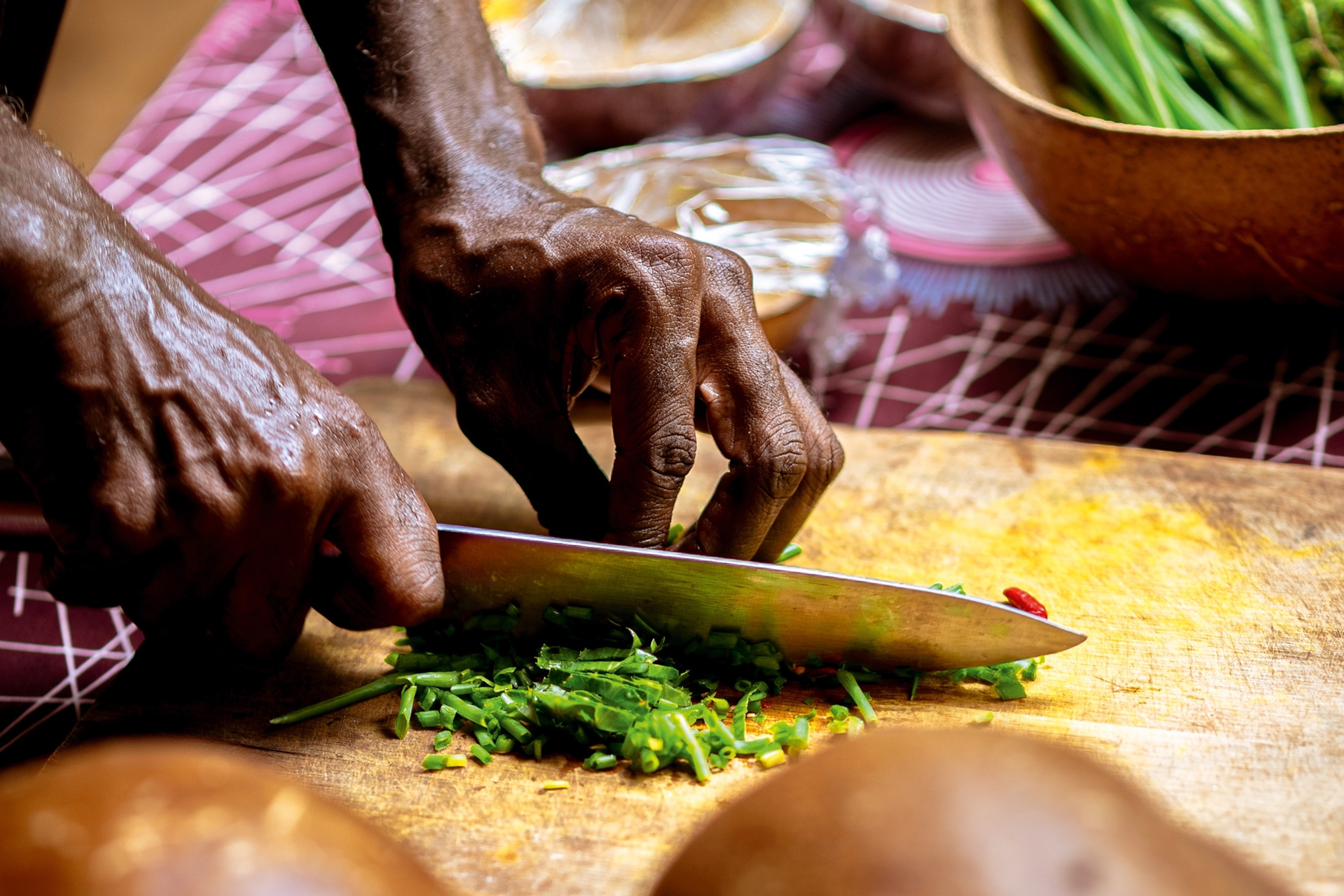 A man's hands chopping up herbs with a knife on a wooden cutting board.
