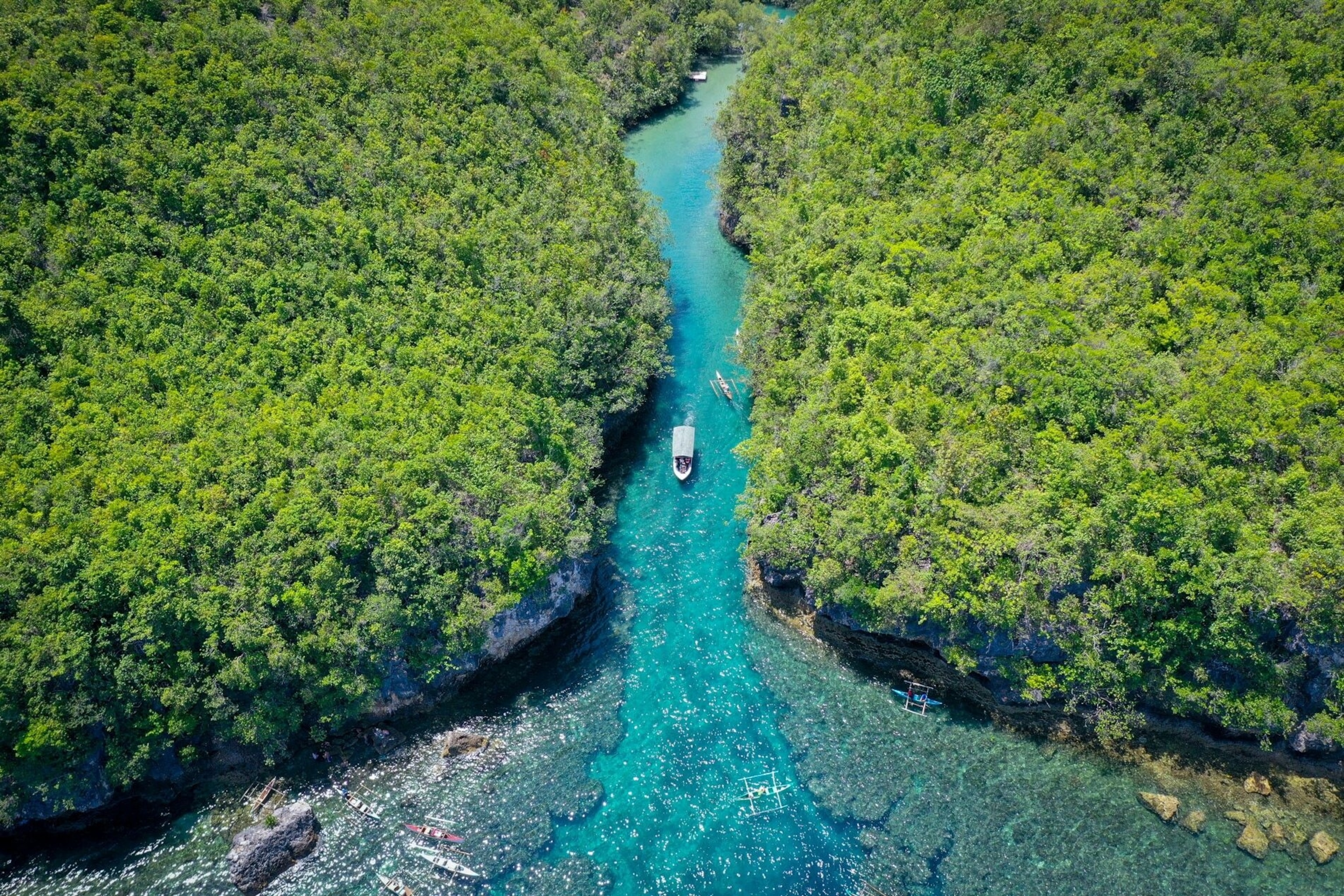 A river cruise along the Bojo River, Cebu. The river glows blue. It snakes between two banks, dense with vegetation.
