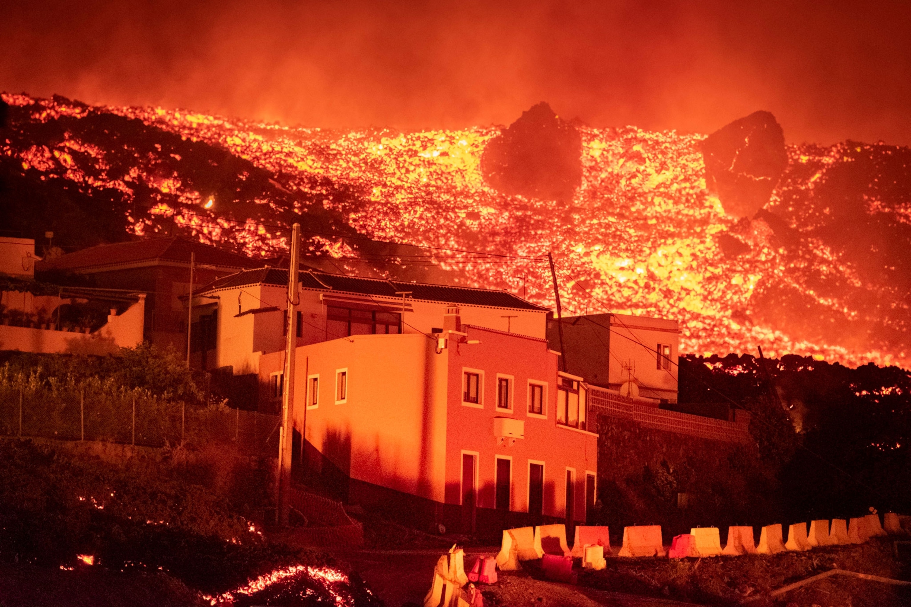 Lava flows and burns on the hillside behind a house.