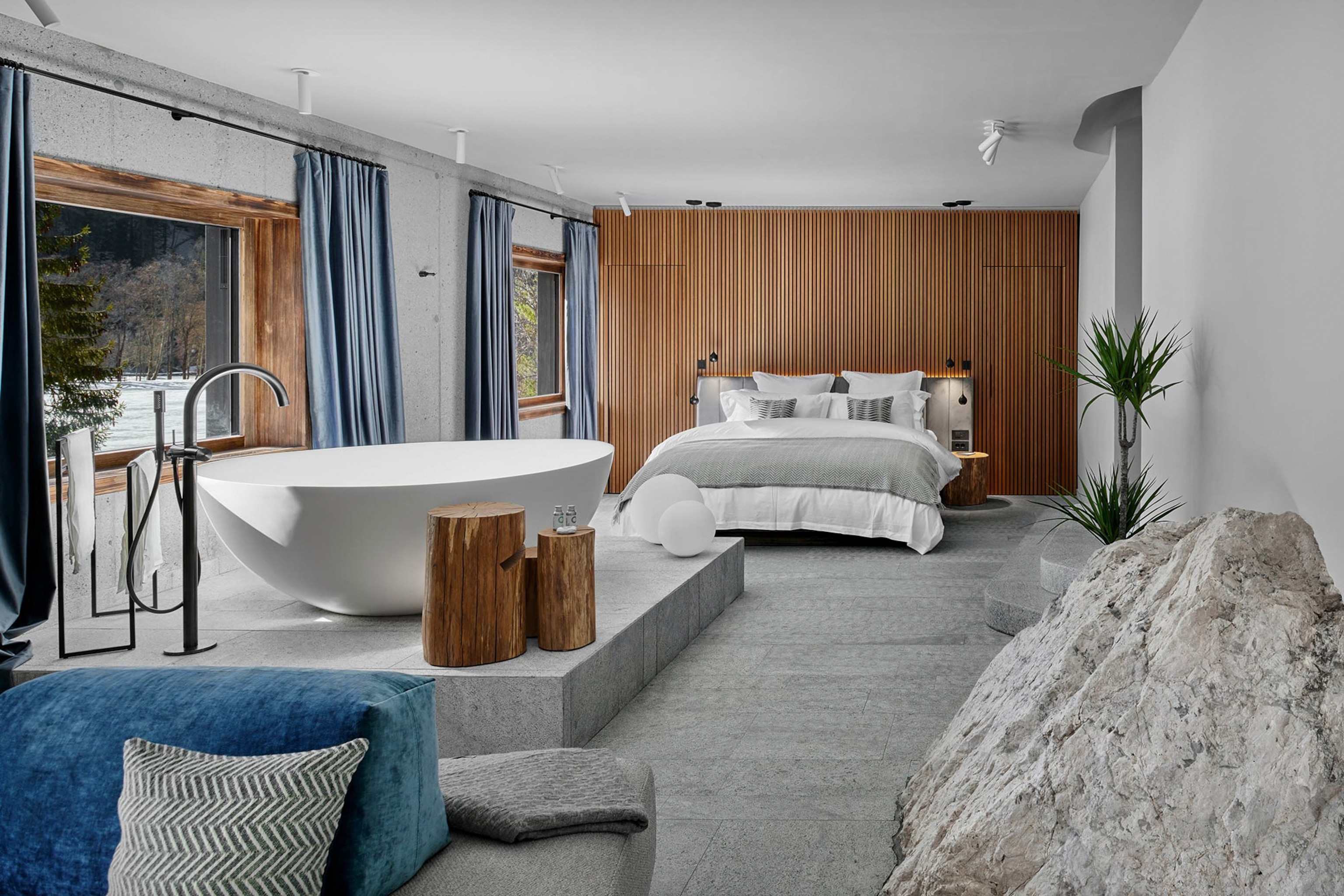 A modern contemporary hotel room with a statement wooden paneled wall and a standalone bathtub in the centre of the room.
