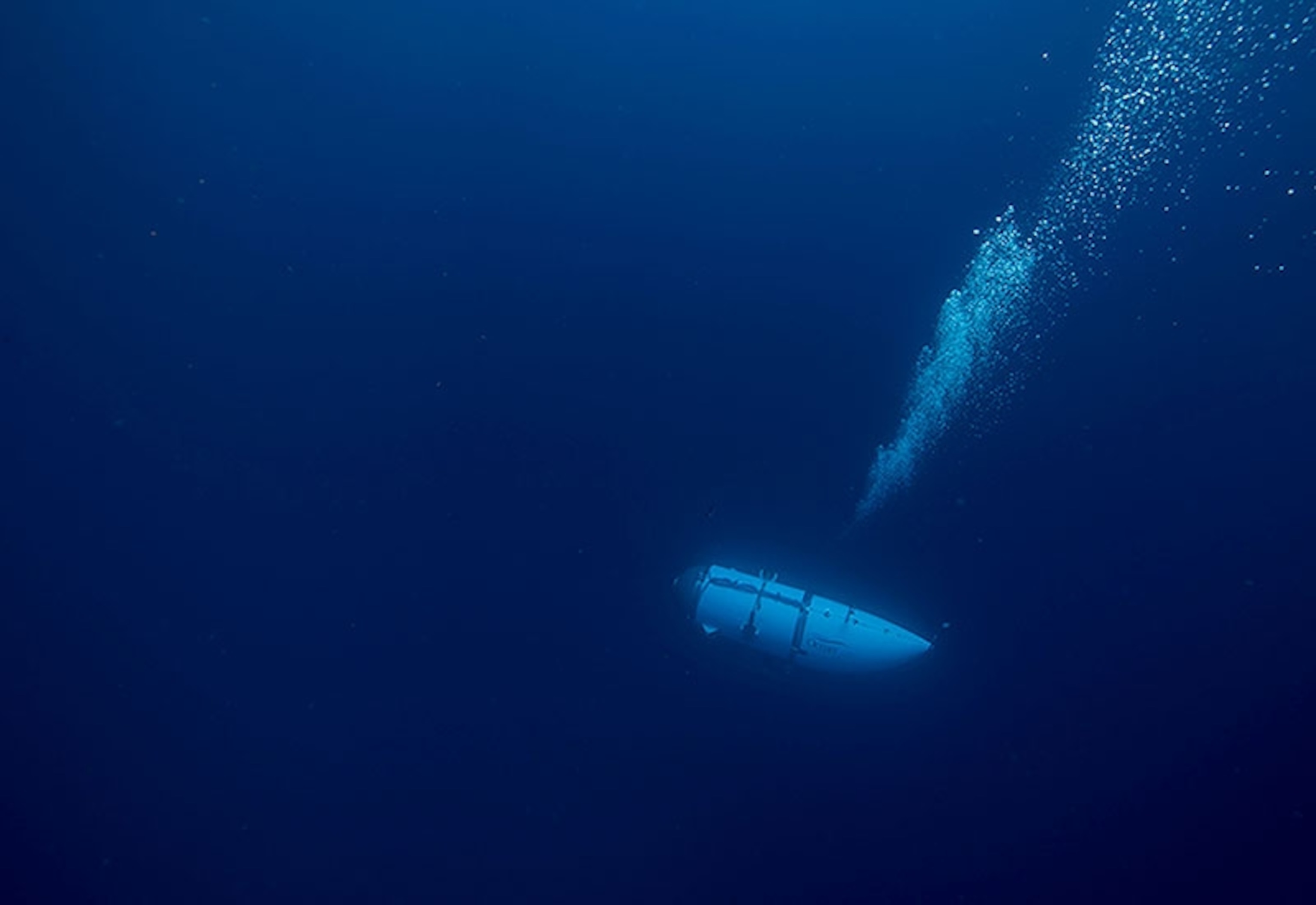 A trail of bubbles follow behind the submarine as it descends into dark waters.