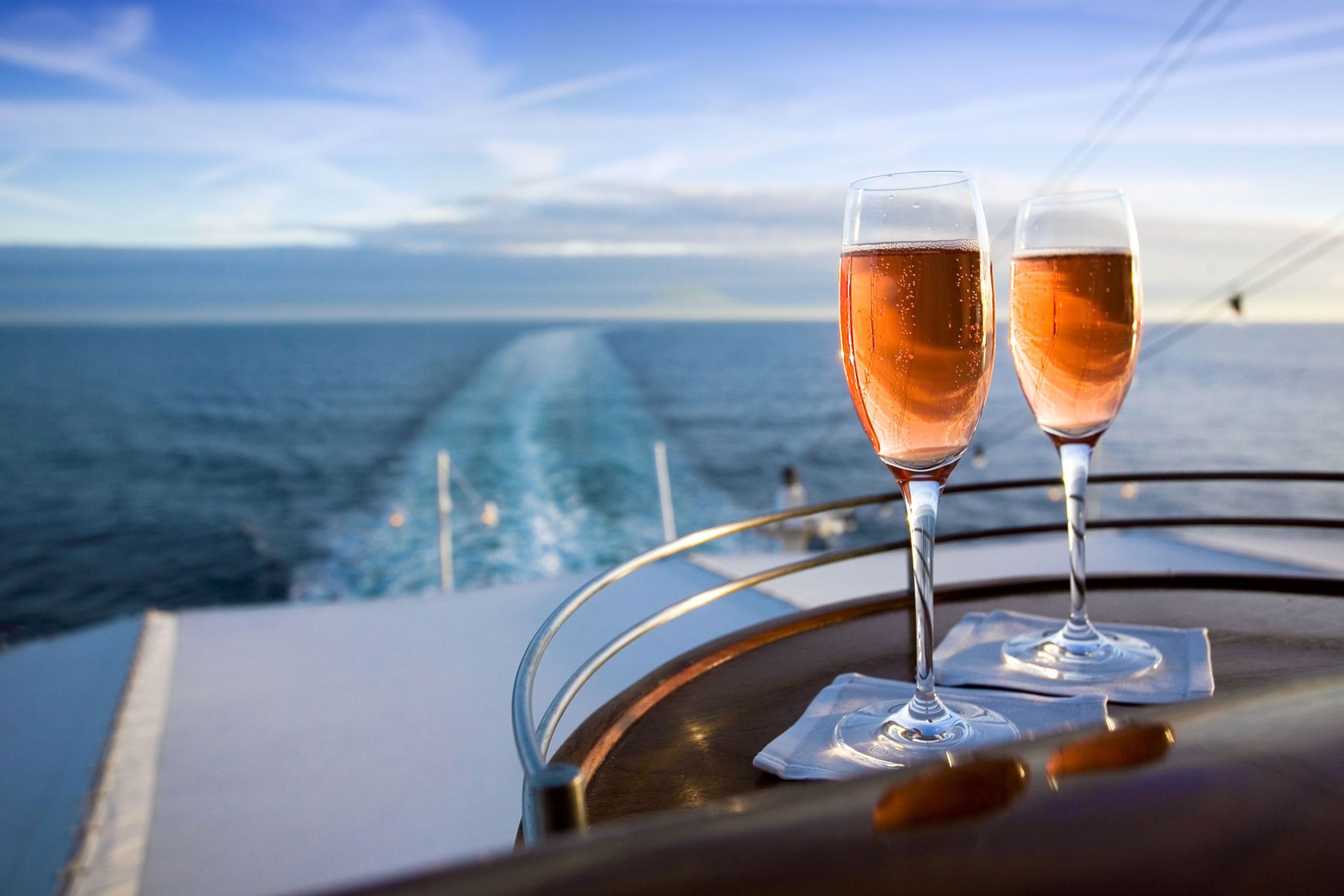 Two glasses on wine sit on a table on a cruise ship deck looking out into the sea.