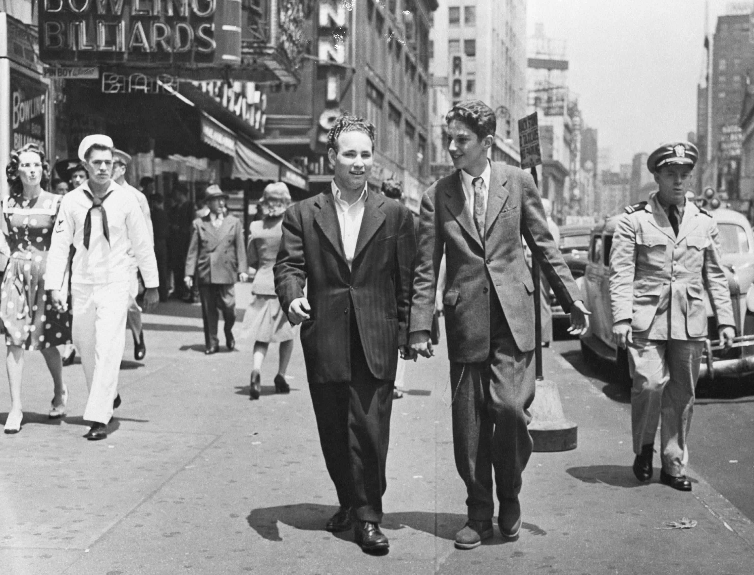 Teenage boys zoot suits walk down a city street in 1943, catching glares and side-eyes from men in military attire.