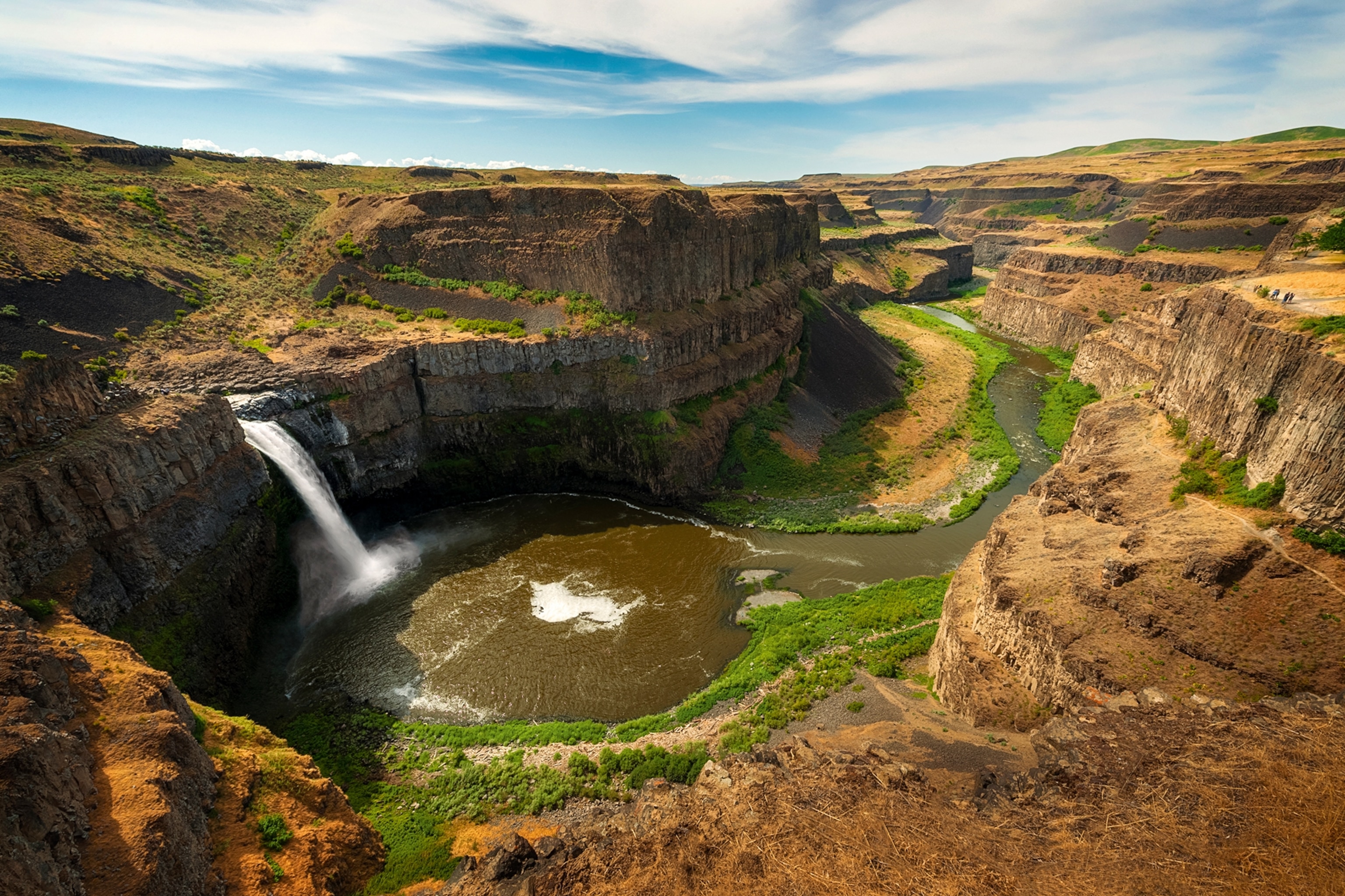 A birds-eye view into a green-rimmed canyon with a waterfall on the side, snaking from a pool down the middle of the canyon.