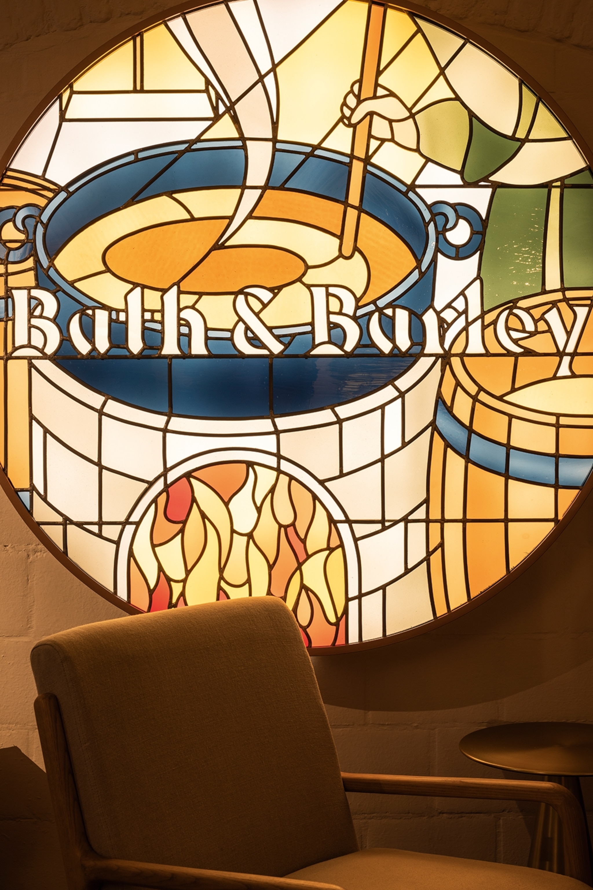 A traditional stained glass window with a person stirring a hot bath barrel.