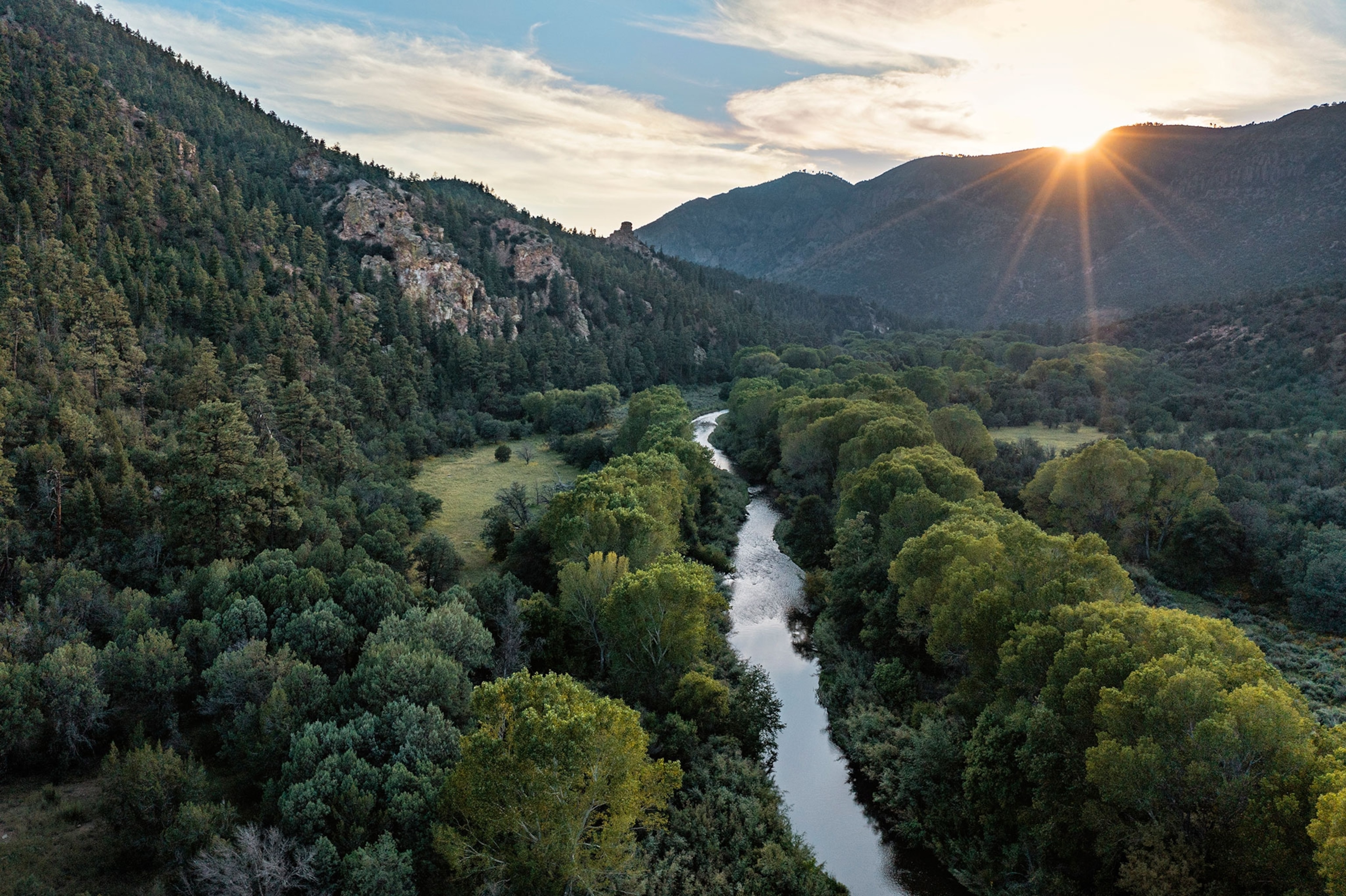 Aerial image of lush mountains with river running through the middle during sunset.
