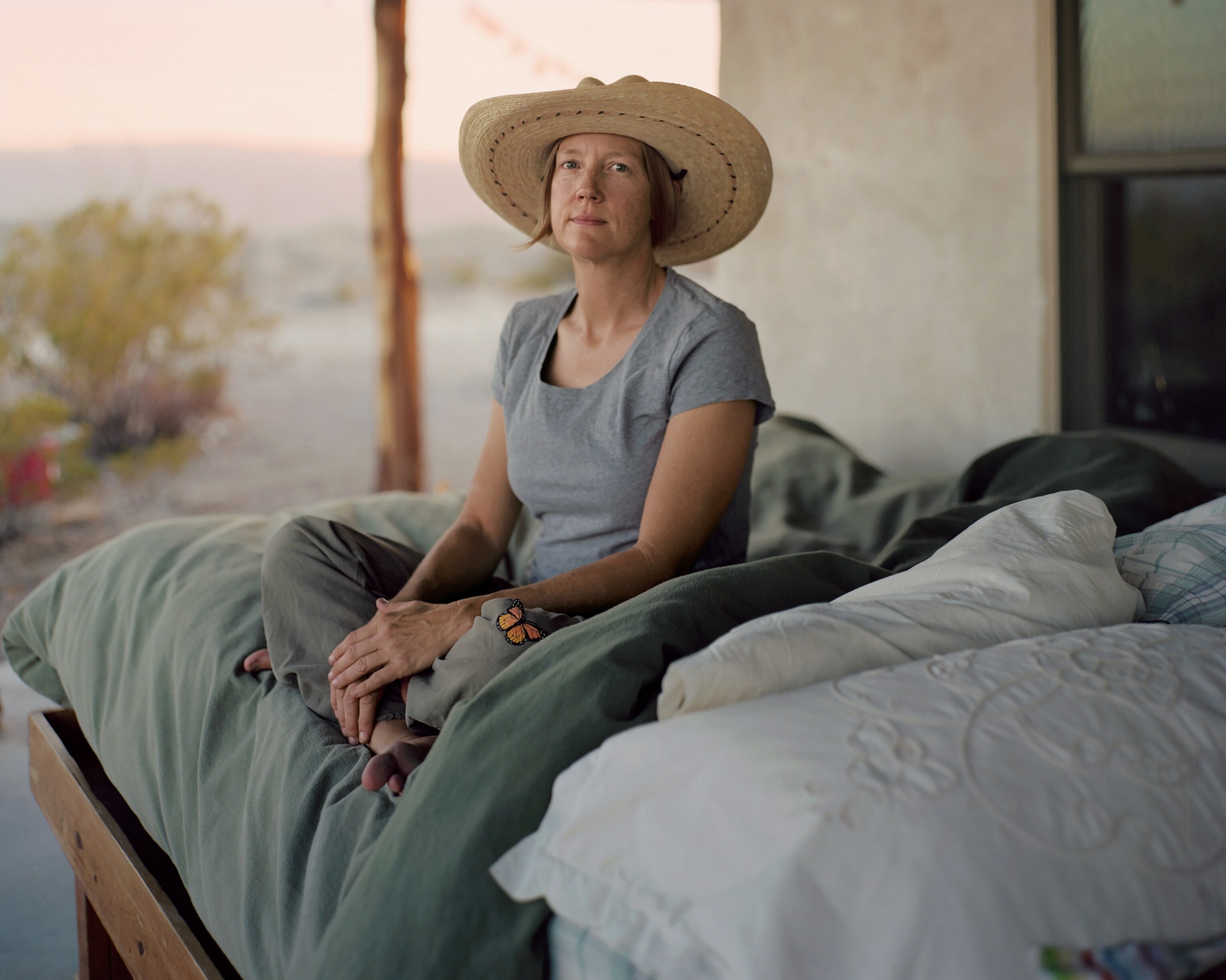 Picture of young woman in straw hat sitting on the bed.