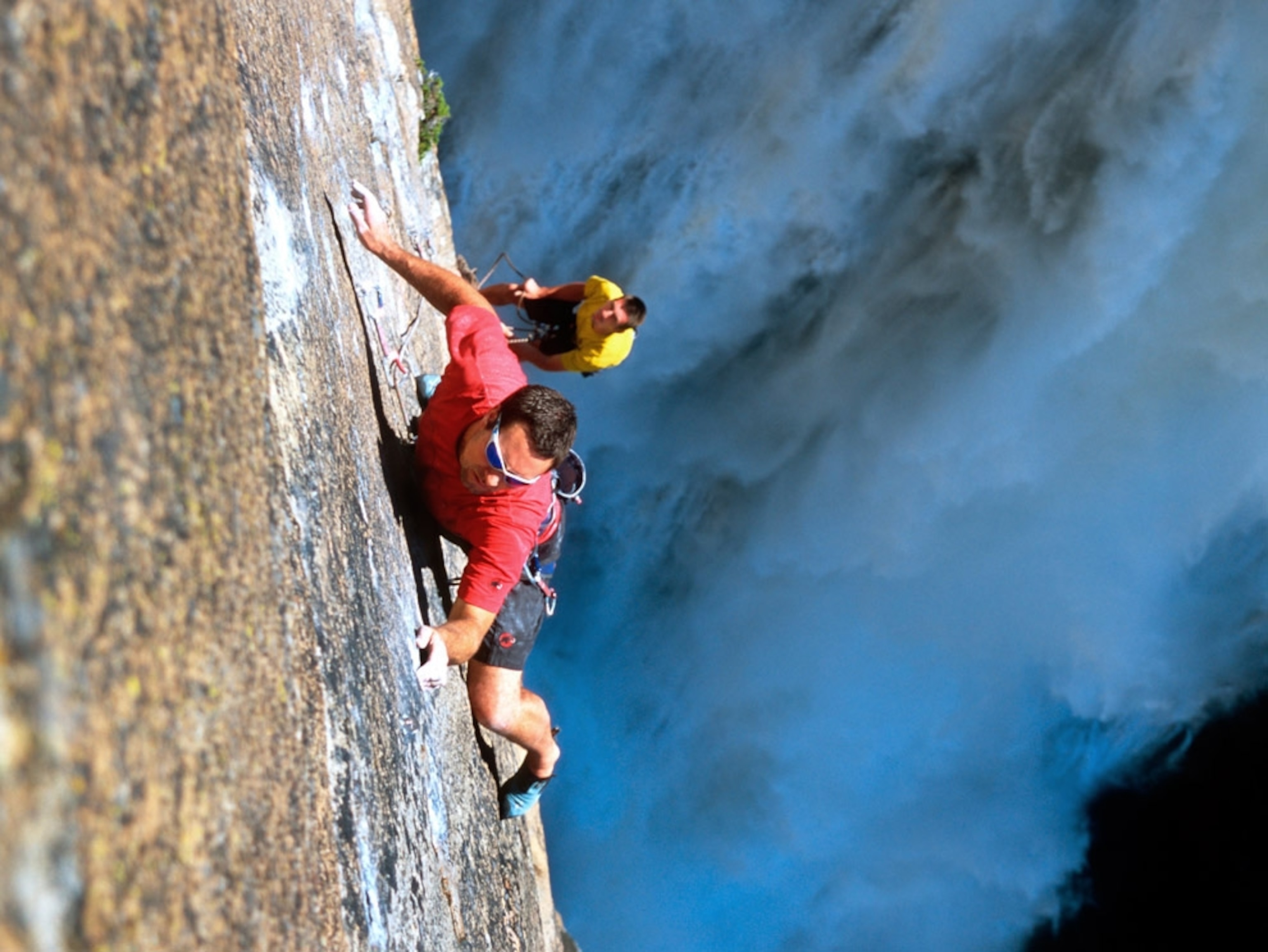 Climber scales rock face overlooking waterfall