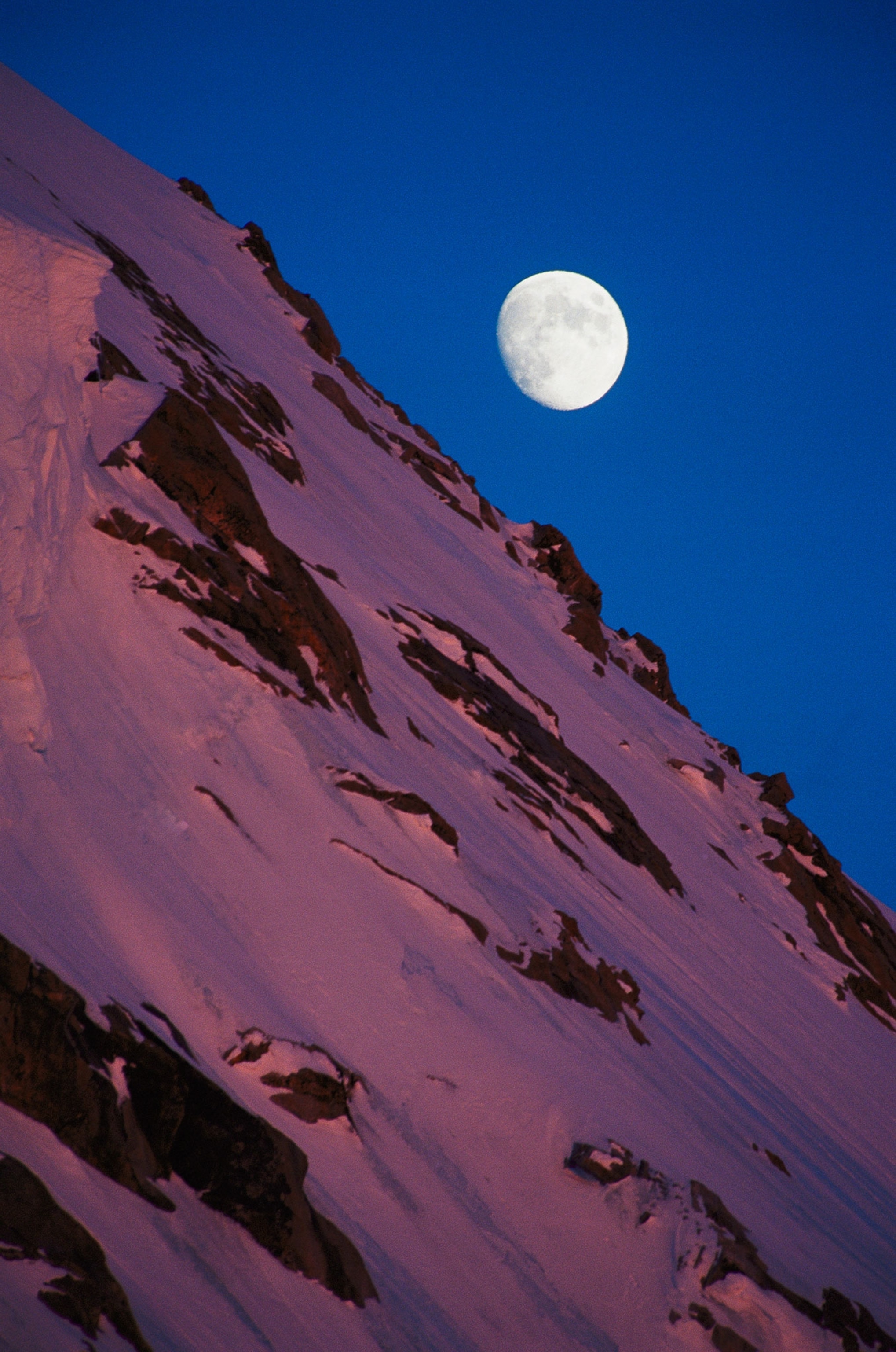 A gibbous moon rising over a snow-covered slope in Denali.