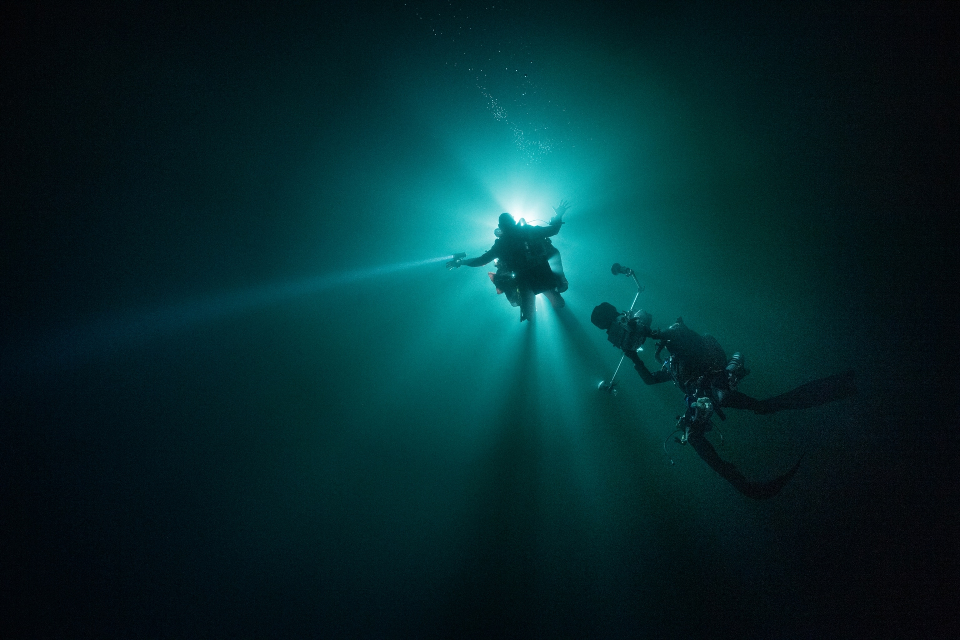 Two backlit divers entering a black hole.