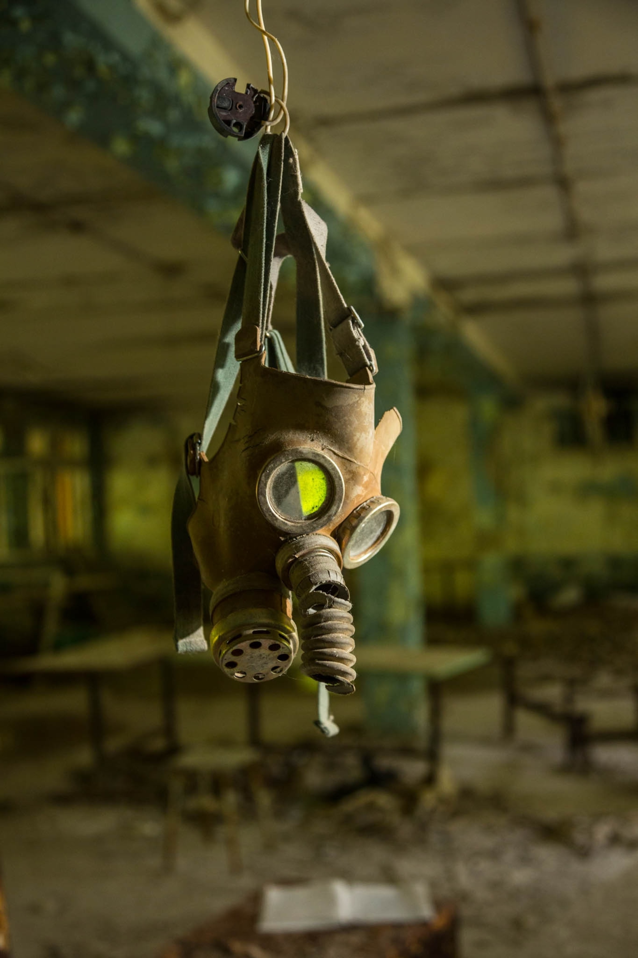 An old gas mask hanging in the ruins of an abandoned classroom.