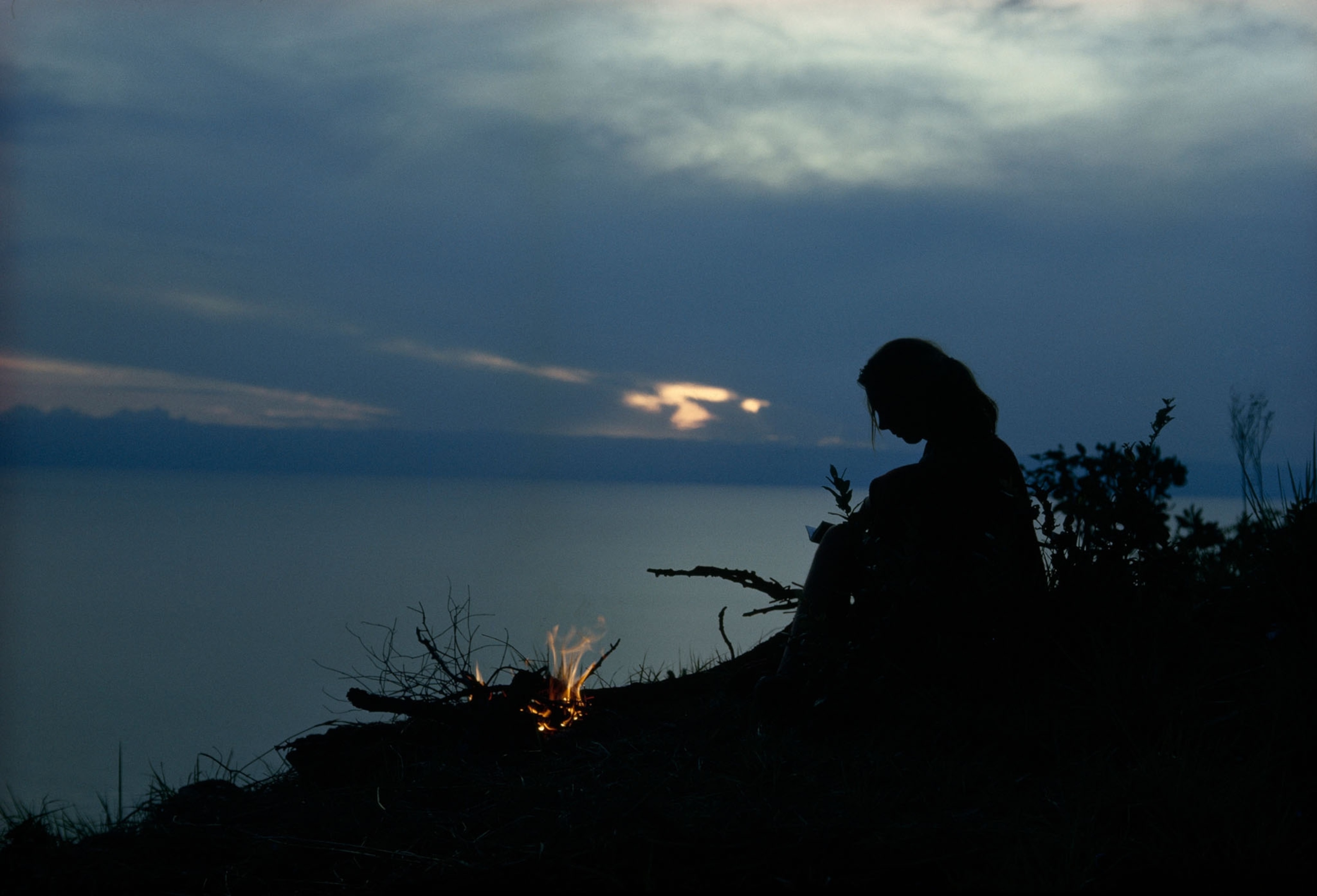 Jane Goodall sitting by a fire on a cliff at dusk