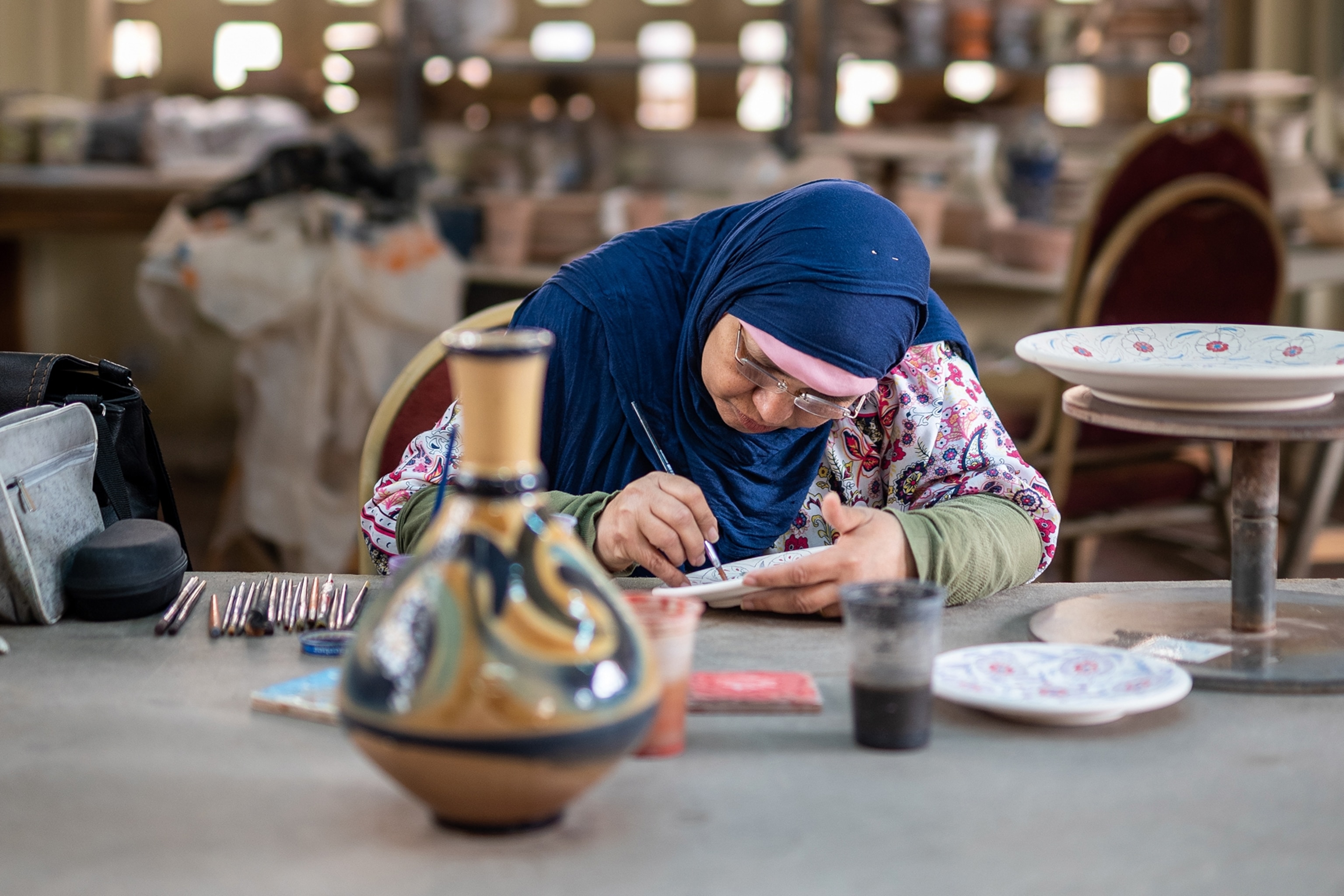 an artisan at at the centre painting a floral design onto a dish