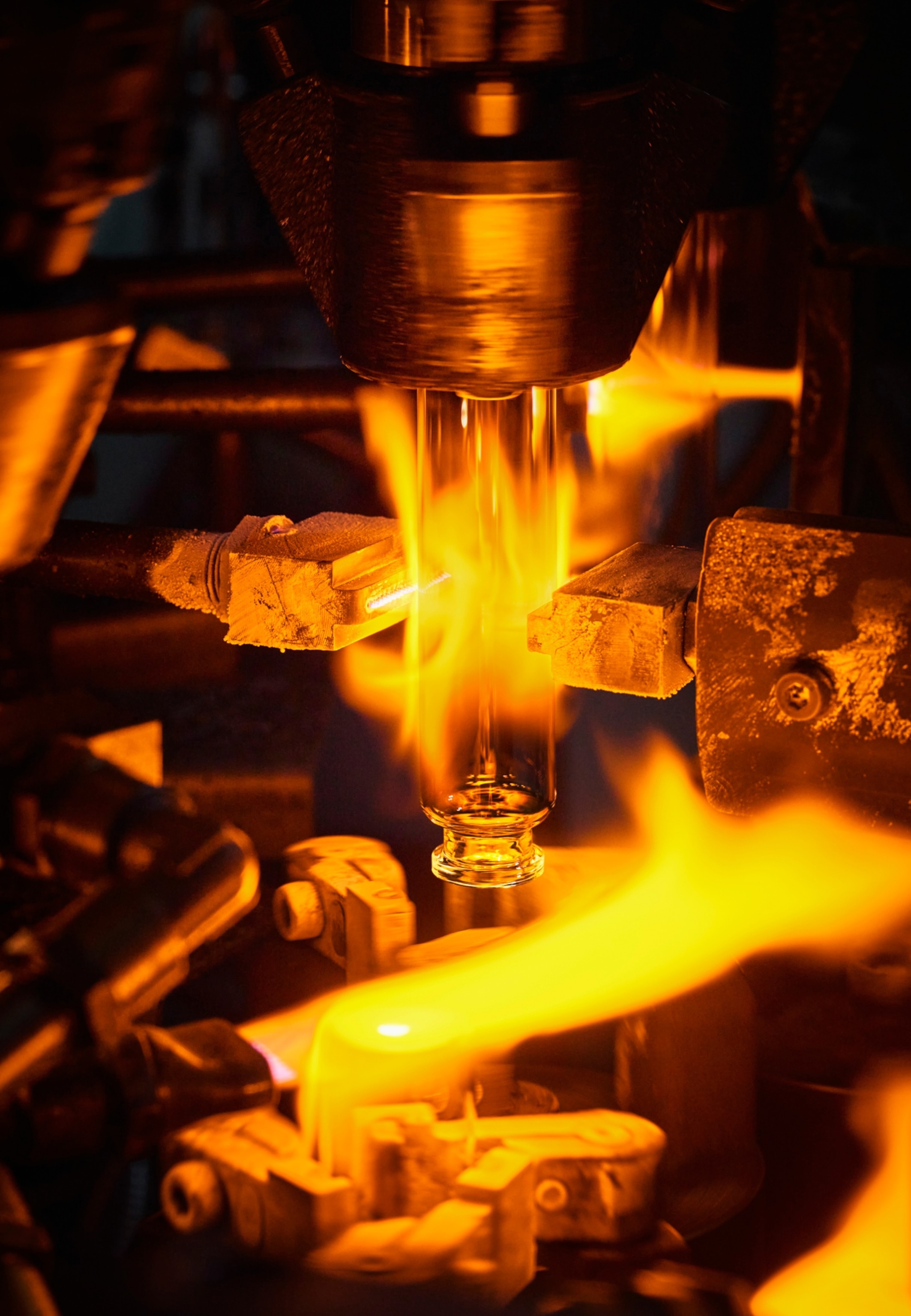 a glass vial being held upside down over multiple jets of flame while two metal edges press against it from the sides.
