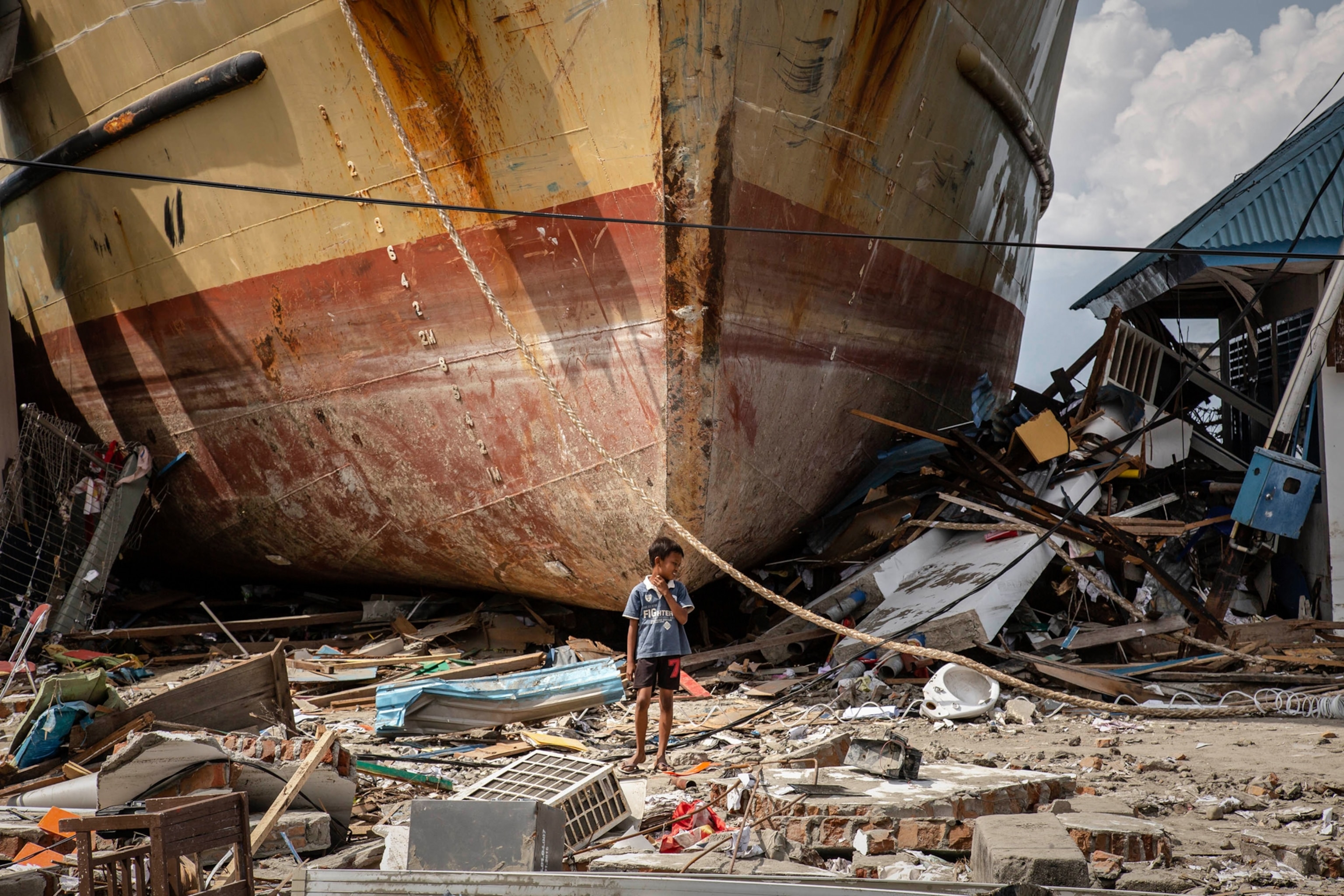 A boy stands in front of a stranded ship after a deadly