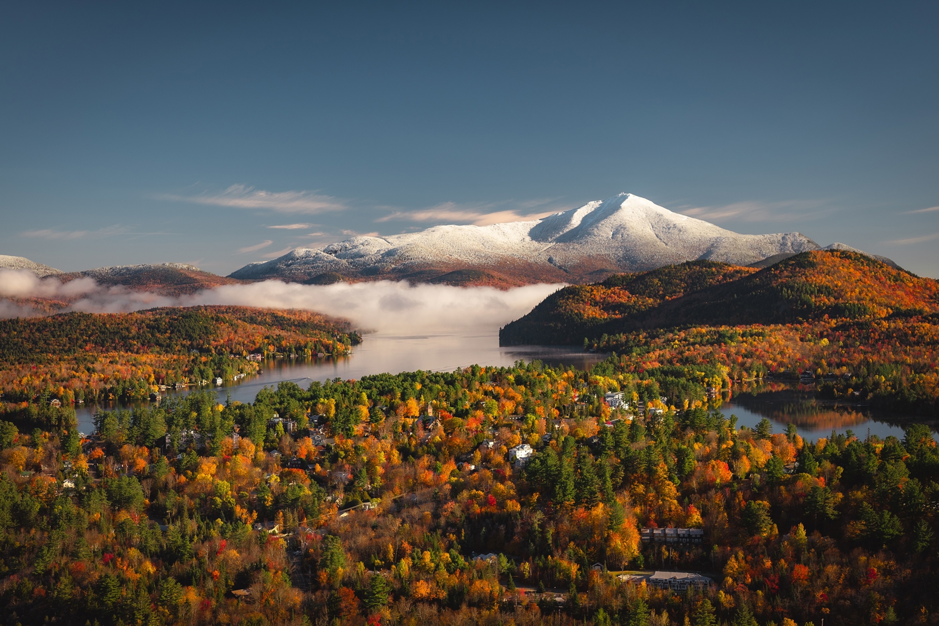 A wide landscape shot from a height of an autumnal forest, a selection of individual lakes and a snow-tipped mountain group.