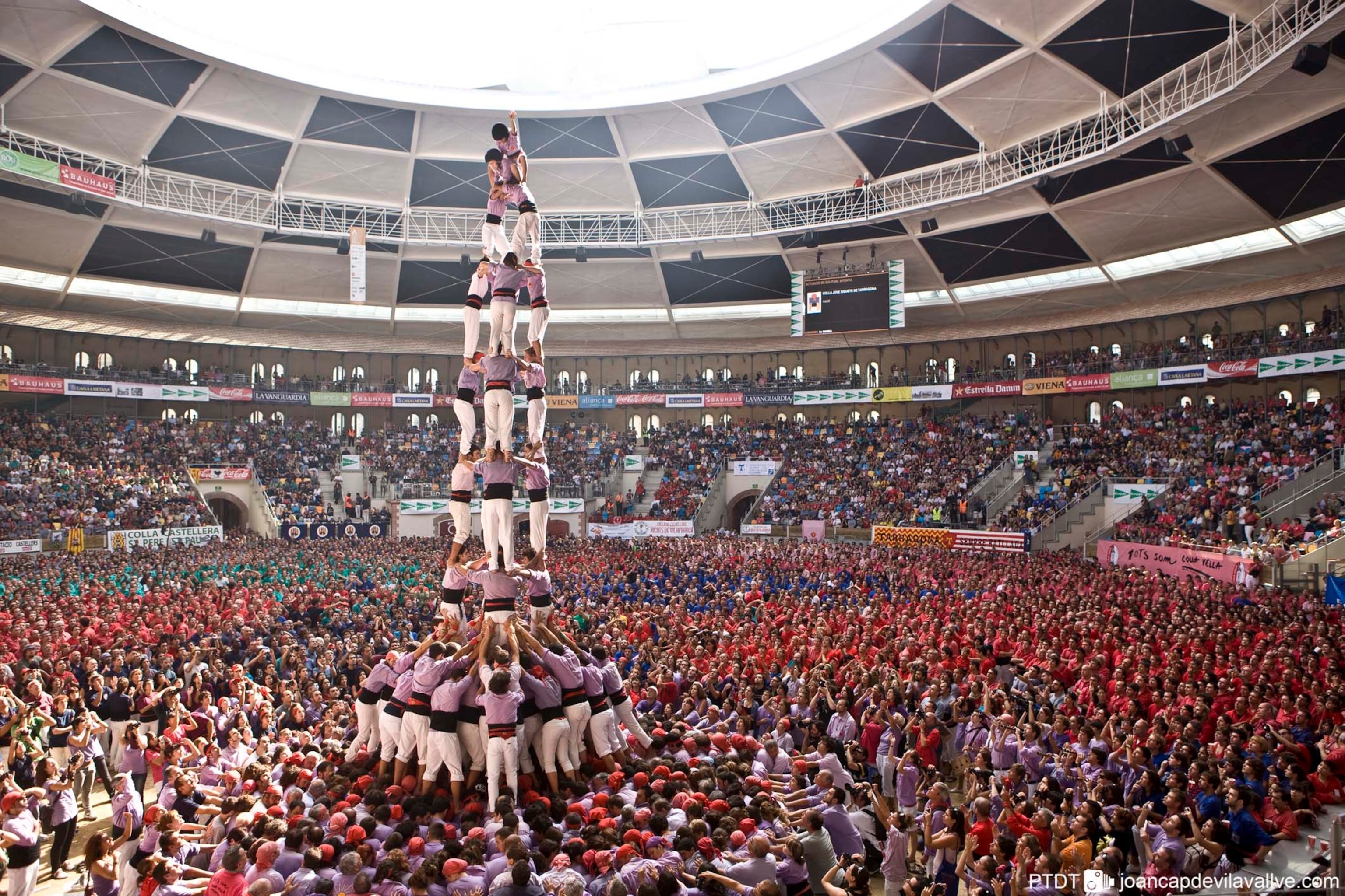 A large crowd dressed in red, at the centre a large tower created from people