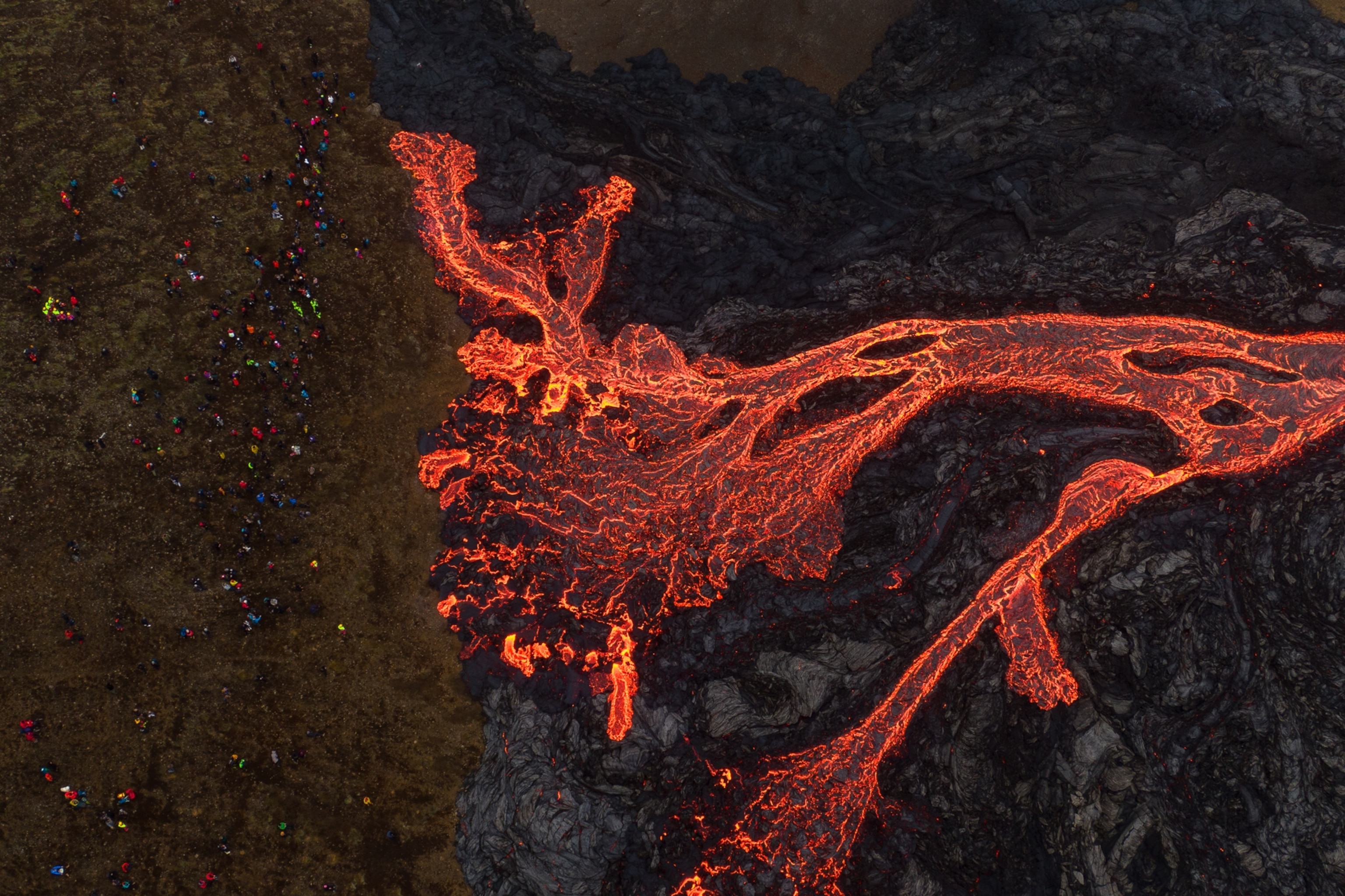 an aerial view of tourists watching lava flow from the volcano