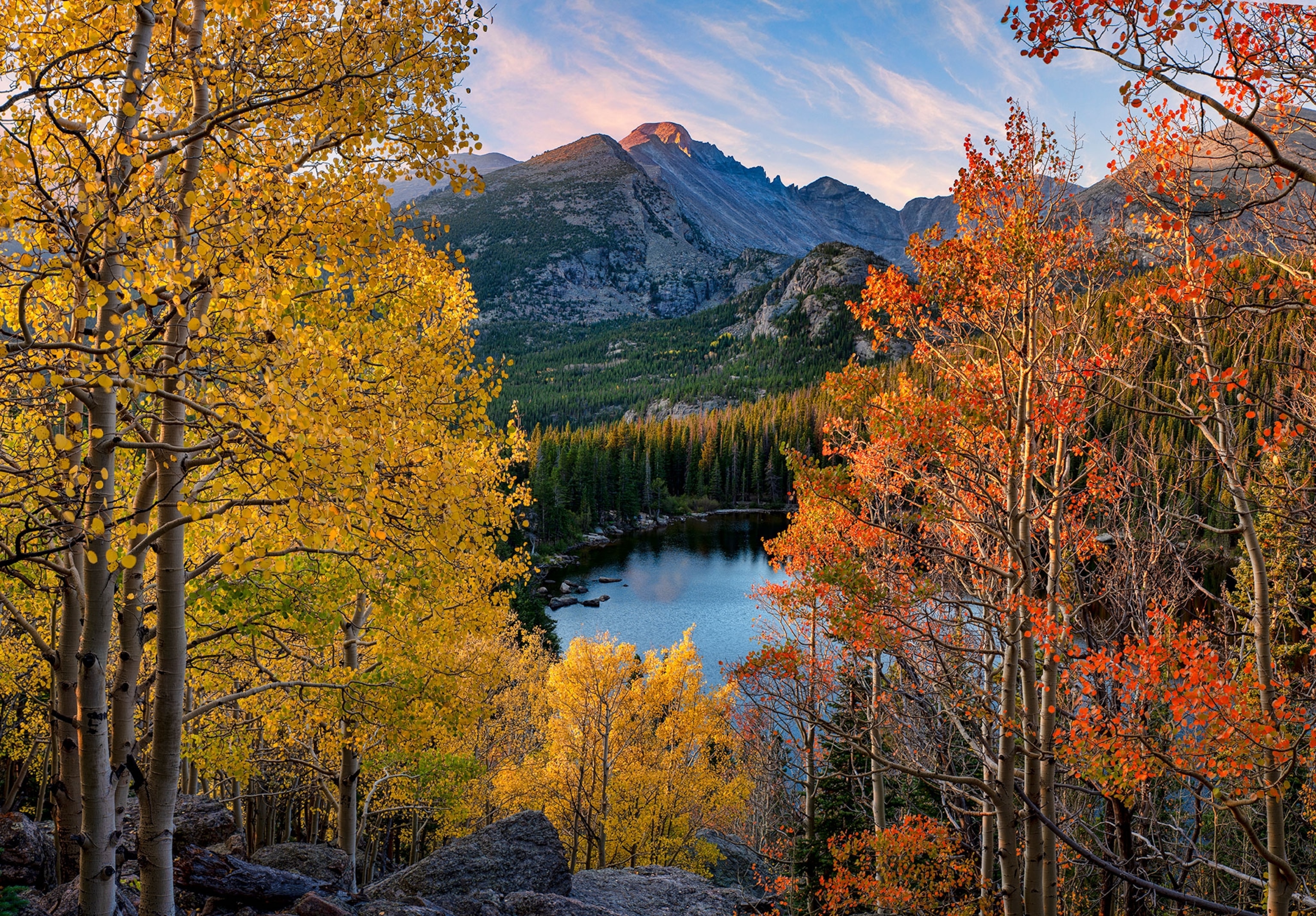 Yellow and orange colored leave filled trees frame a view of a lake below with a mountain in the back.
