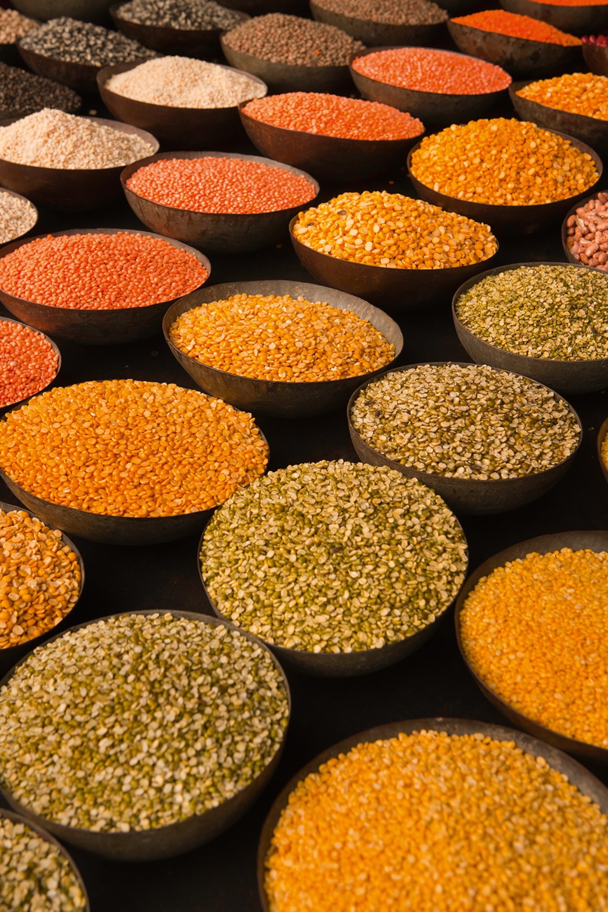 Multiple rows of bowls filled with different kinds of pulses.