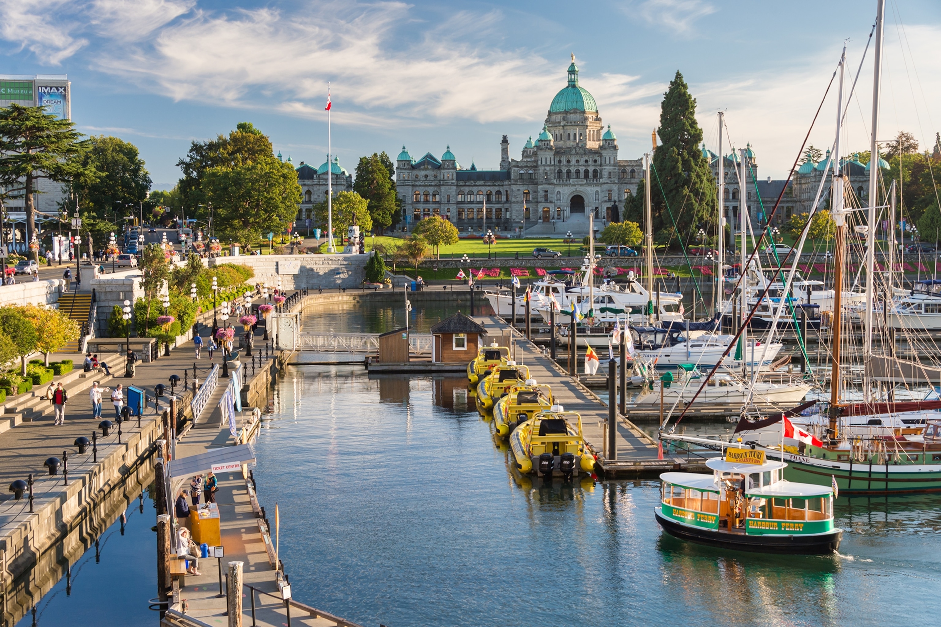 A picture of the central area of Victoria, the capital of British Columbia. The architecture is traditional, and in the foreground sailboats dock in calm waters.