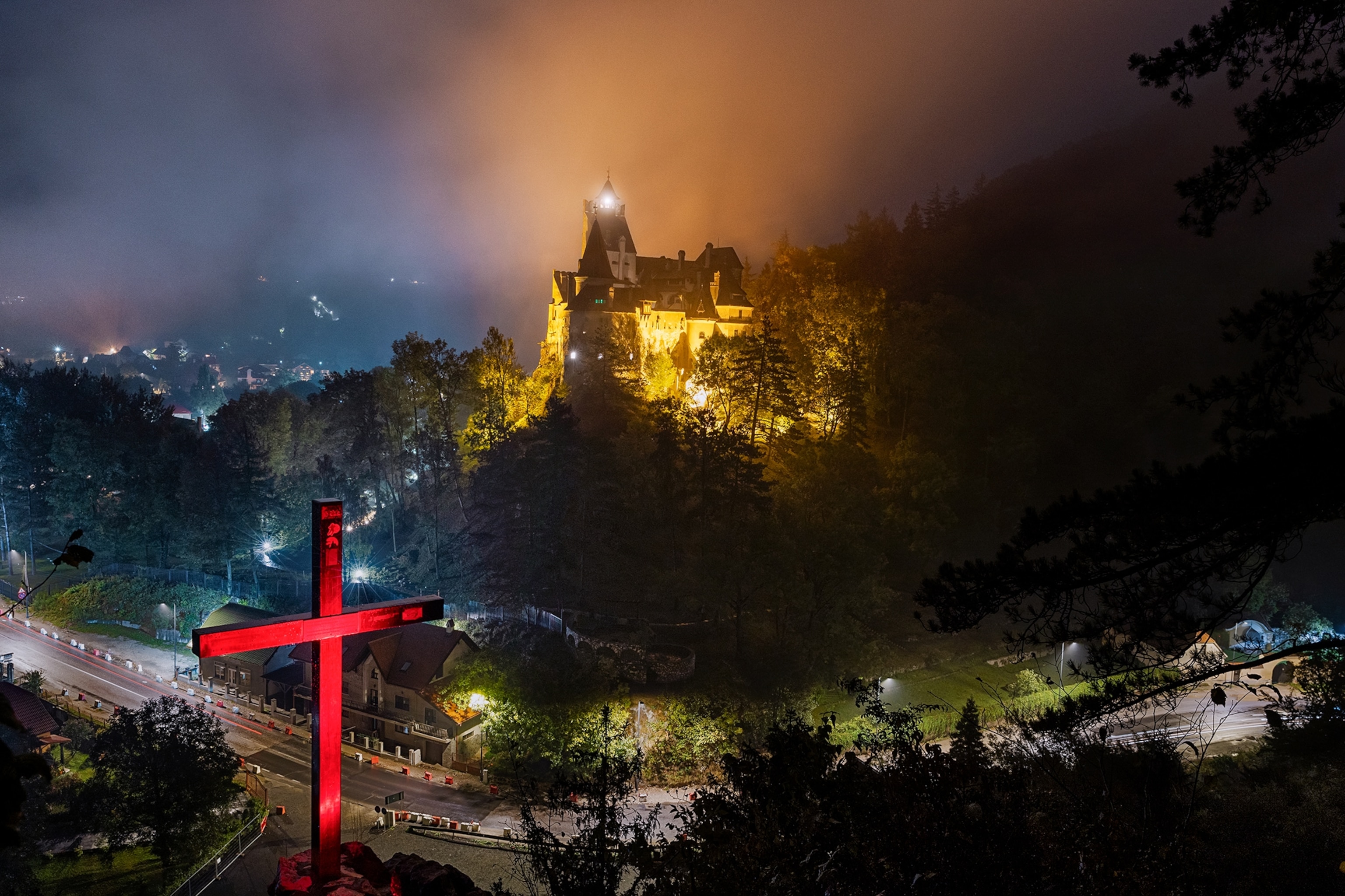 Bran Castle at night with a red cross in the foreground.