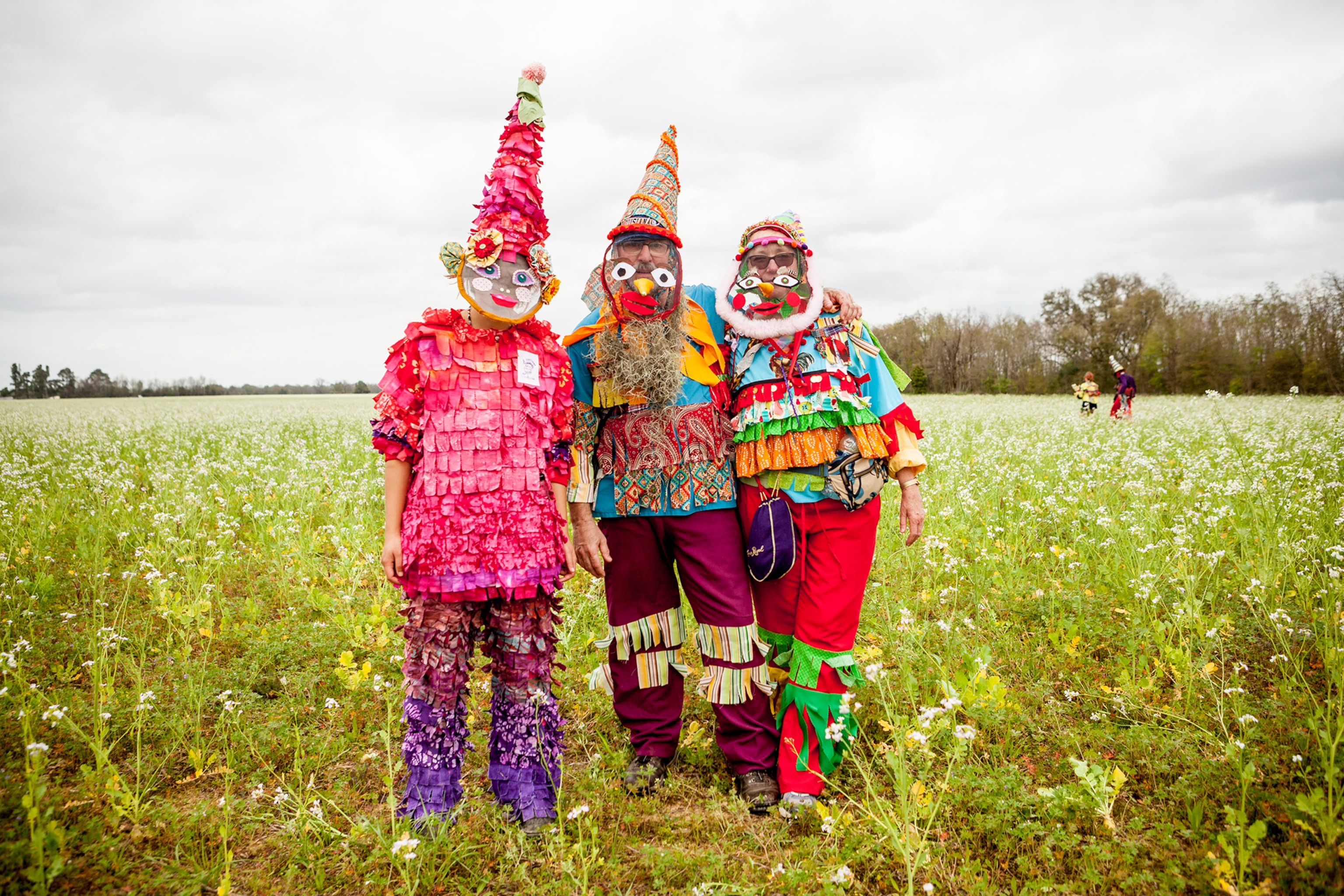 three participants standing in a field wearing costumes at the Courir de Mardi Gras