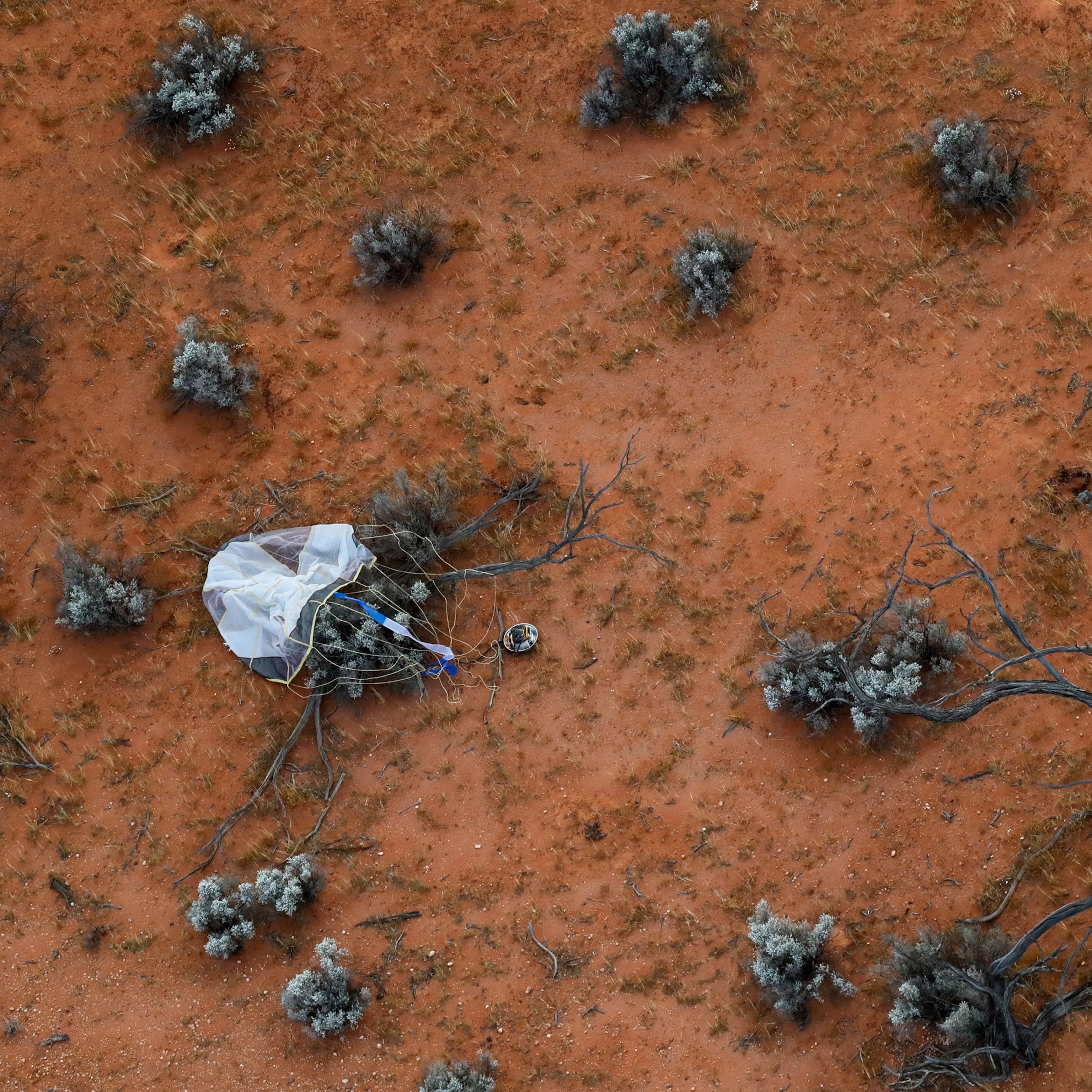 Picture of white parachute with attached container on terra-cotta soil.