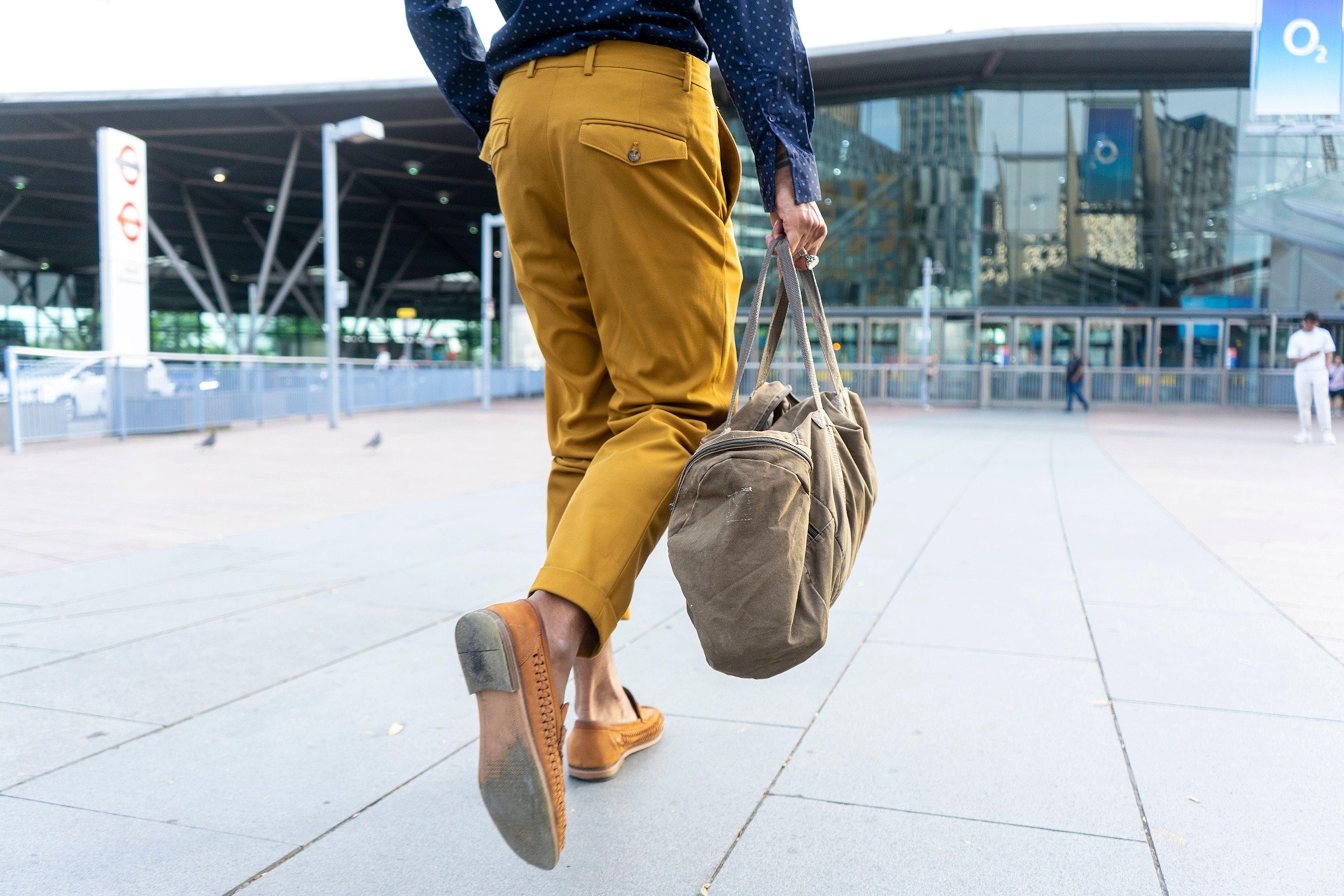 A man with brown shoes and a brown bag walking on a city street.