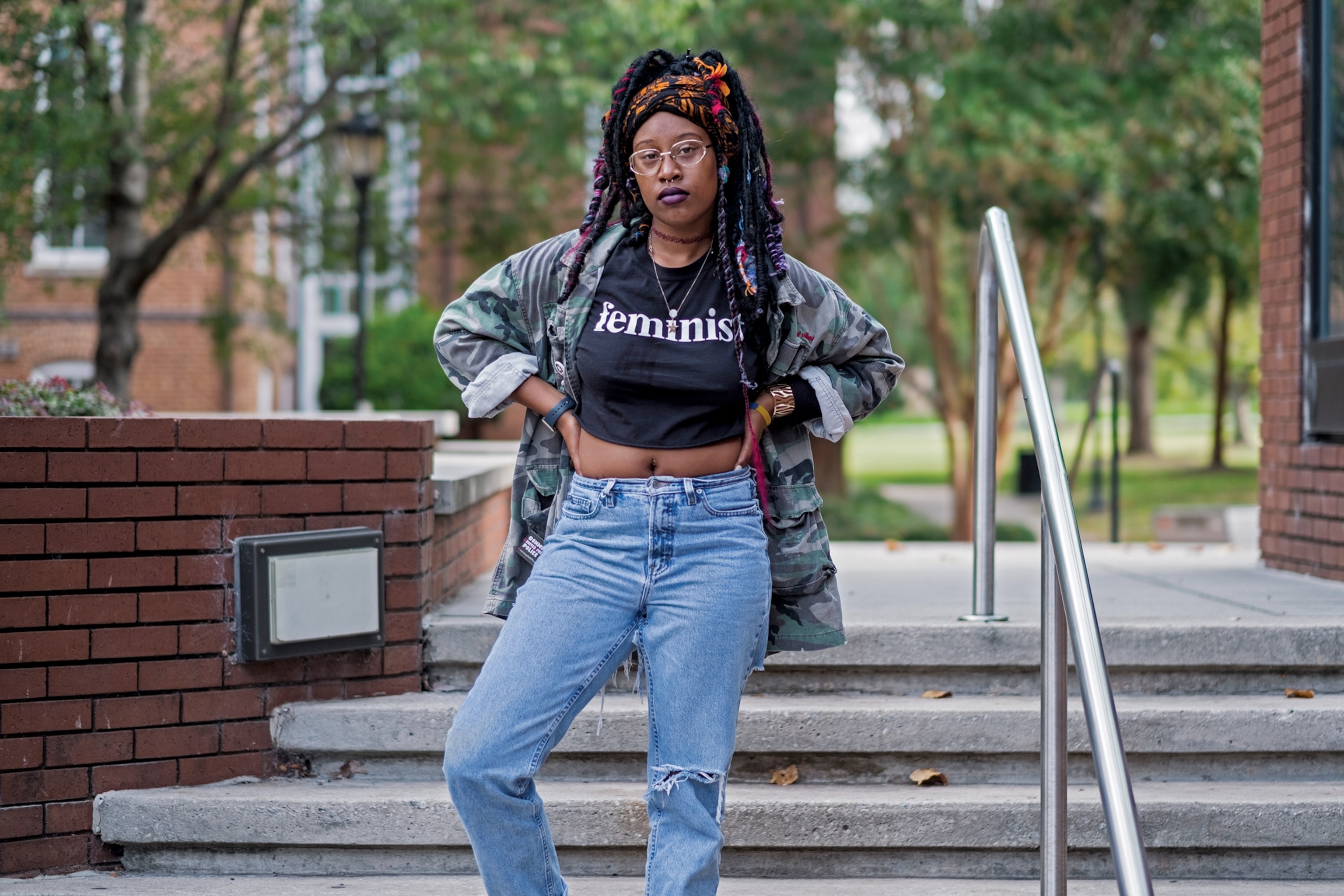 African-American young woman in glasses wearing a T-shirt with feminist sign on it.