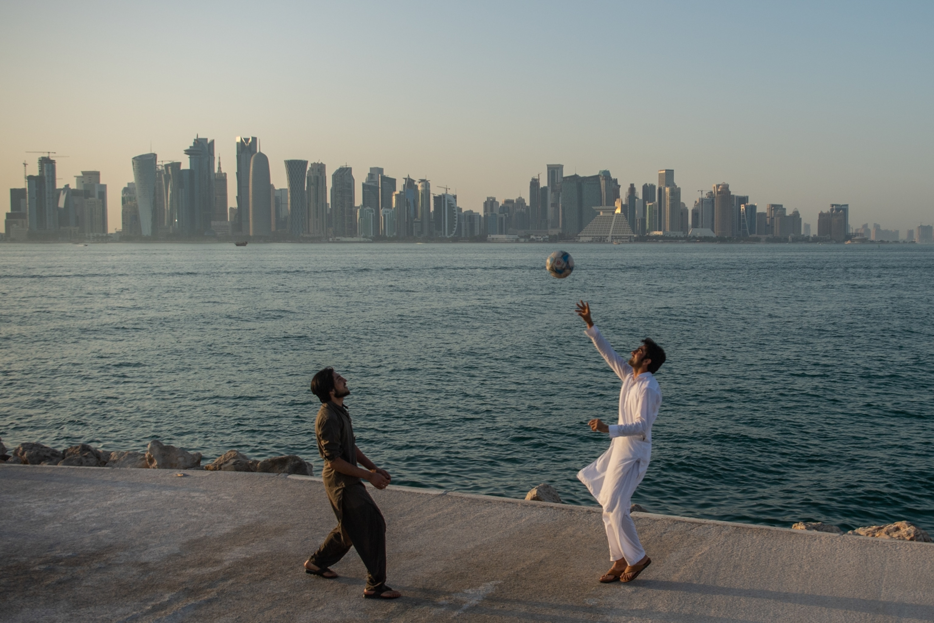 People play volleyball in front of the skyline of Doha