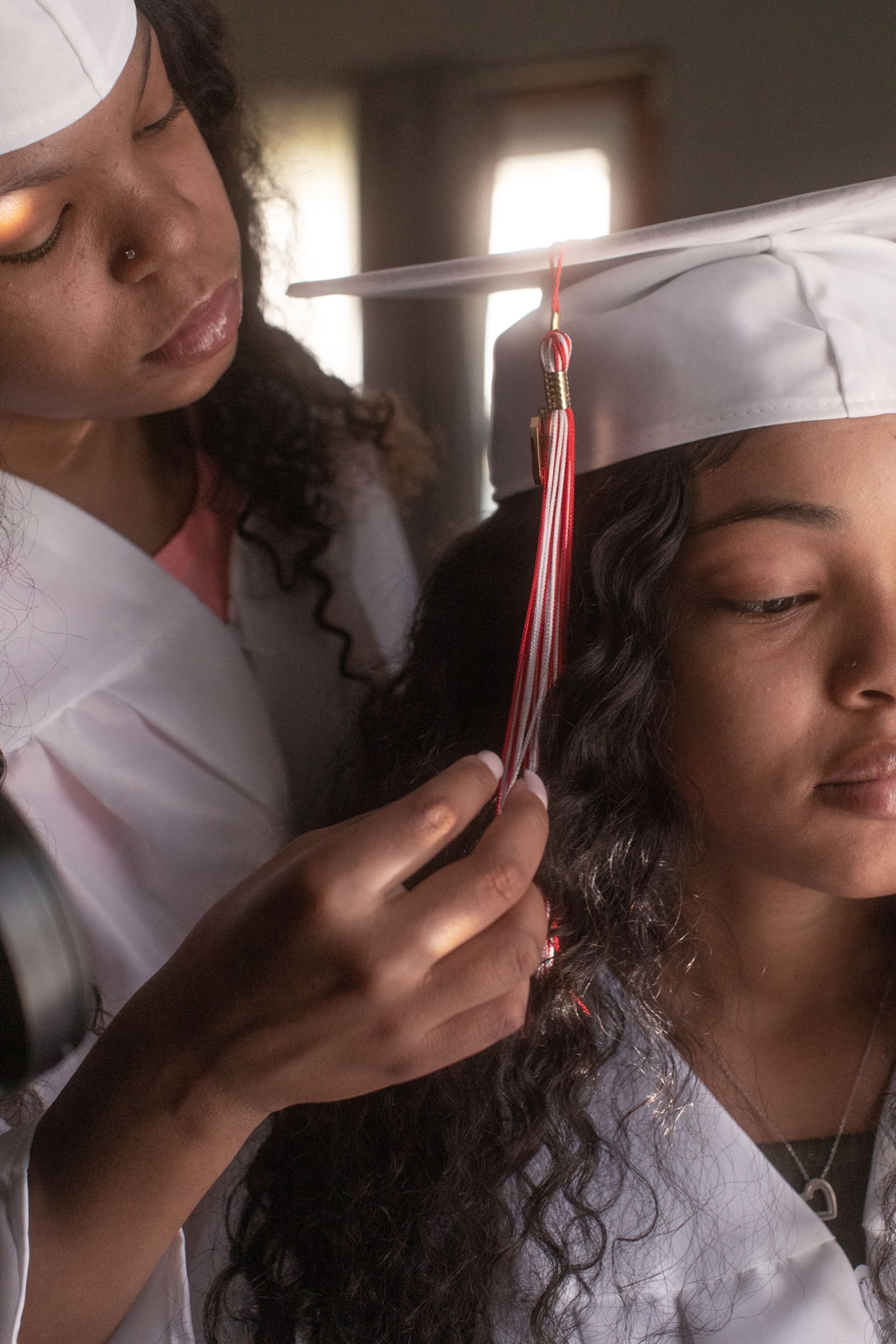 one girl in white graduation robe is fixing another girl's hat.