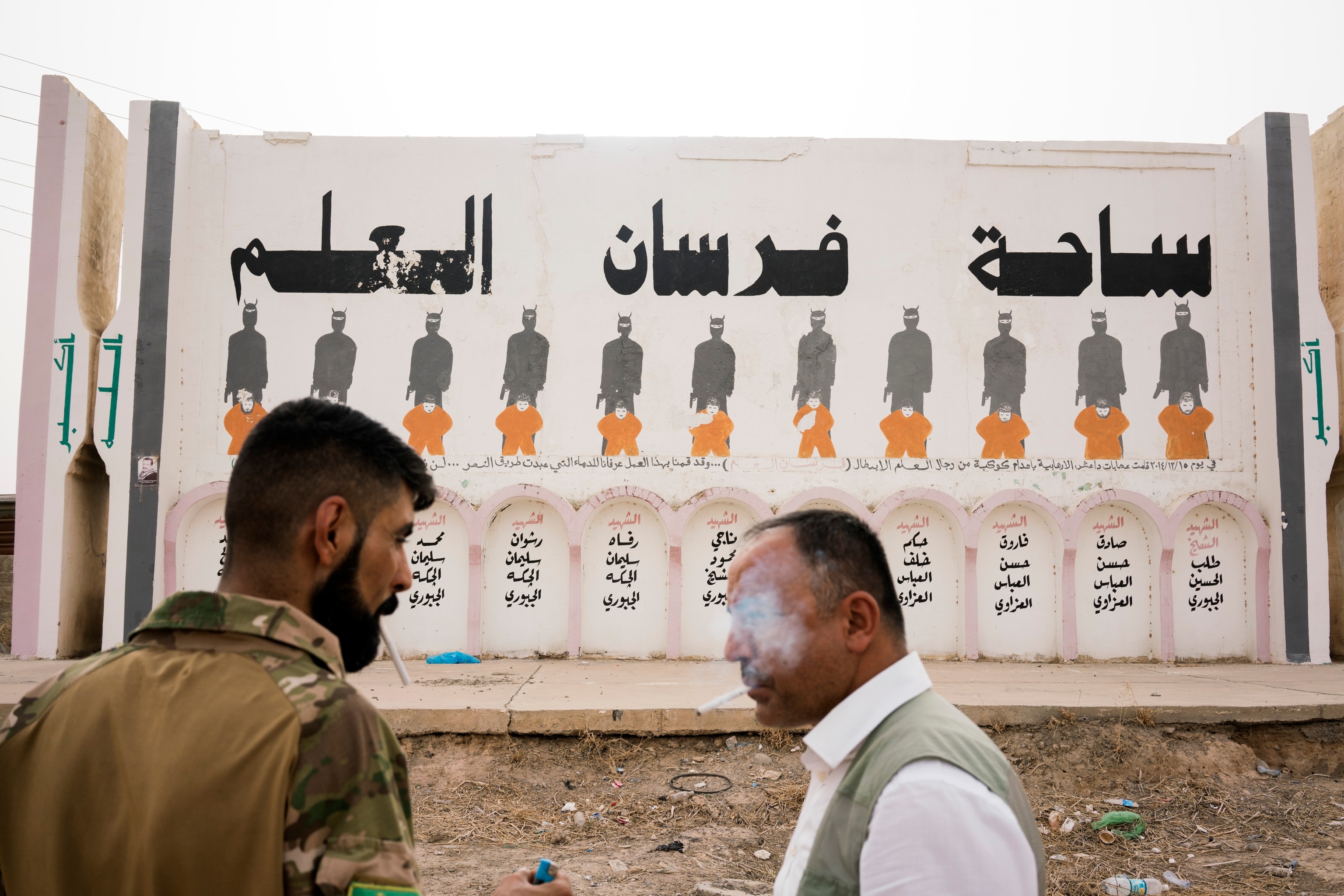 men next to a memorial for civilians killed by ISIS