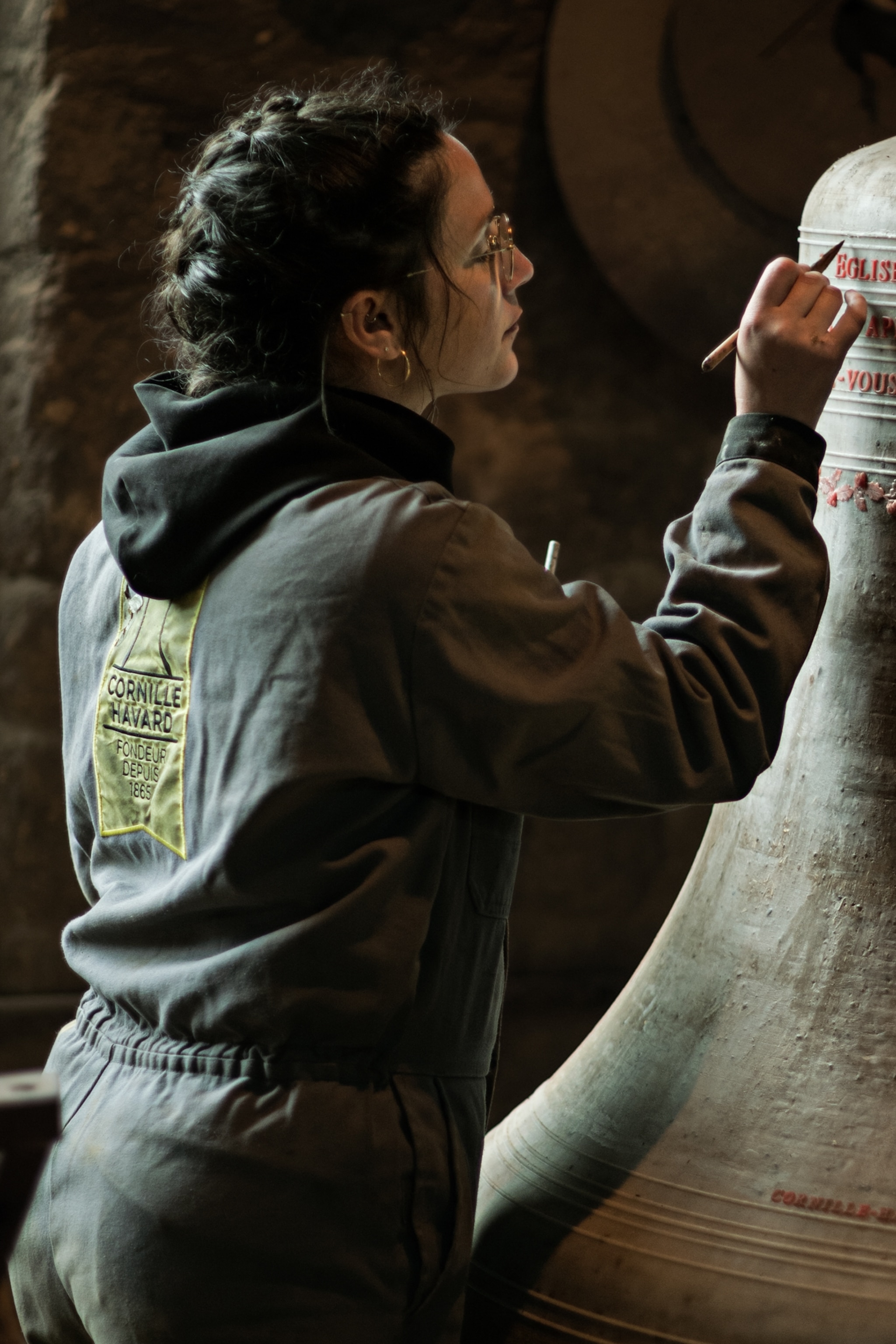 Pauline Desfaudais is standing while painting letters on the top of a bell.