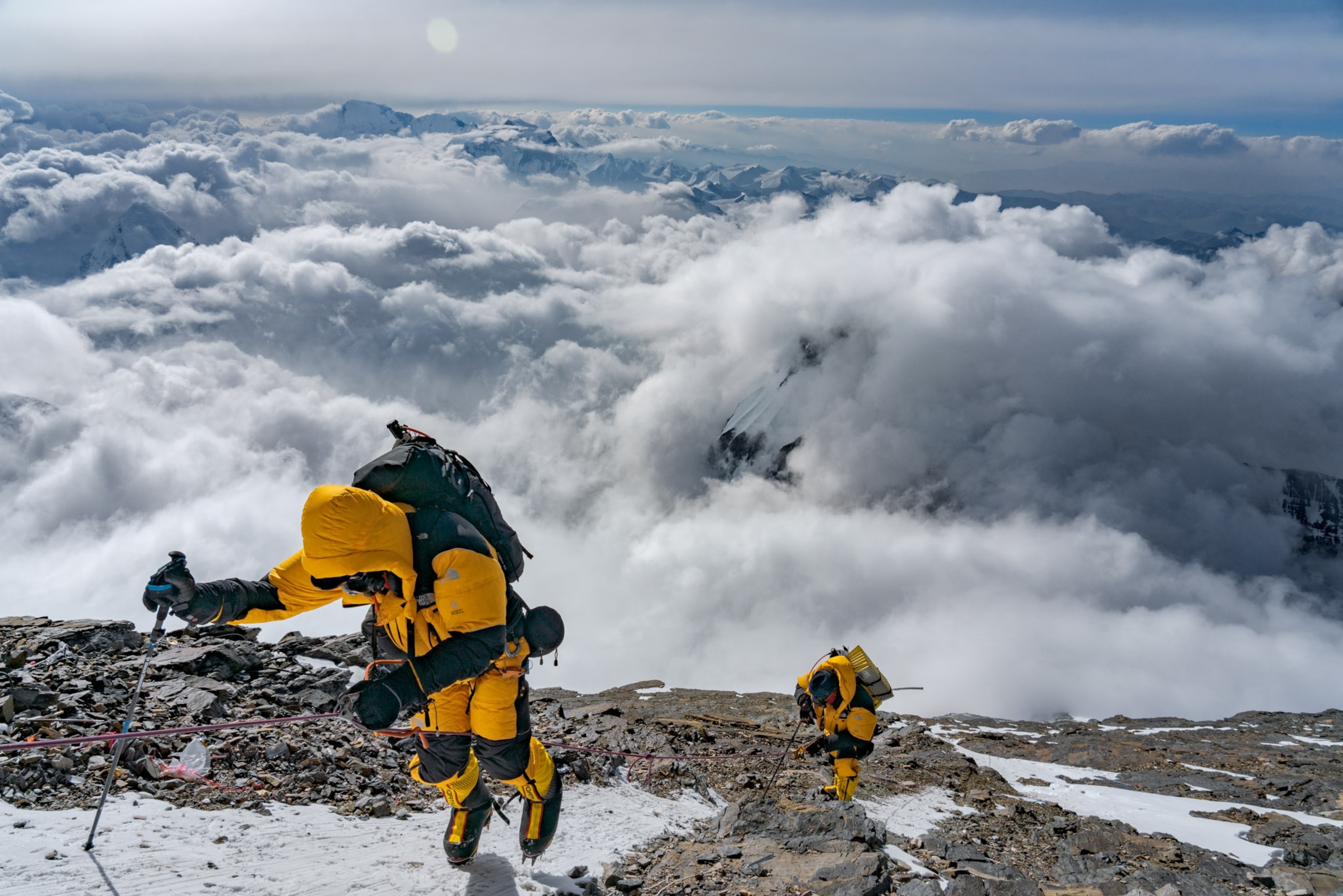 two men in yellow snow suits climbing above the clouds
