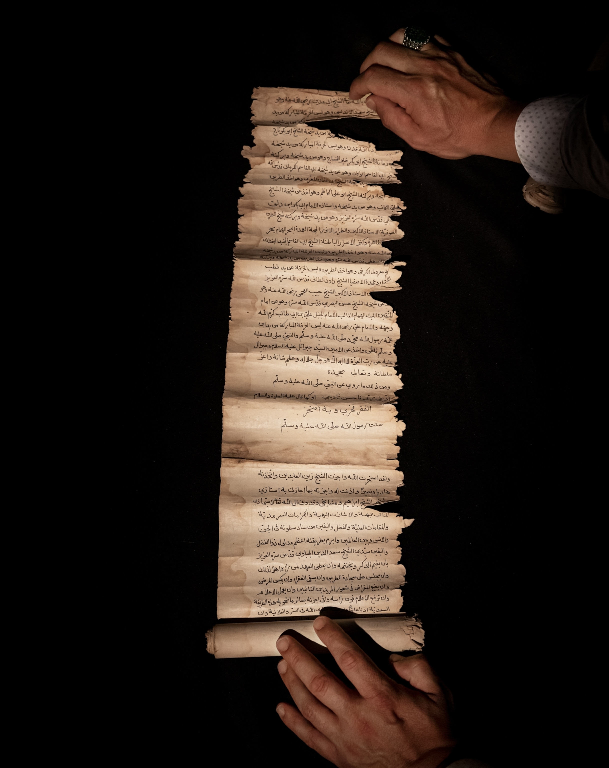Image of an aged and frayed manuscript with written Albanian language gently held open.