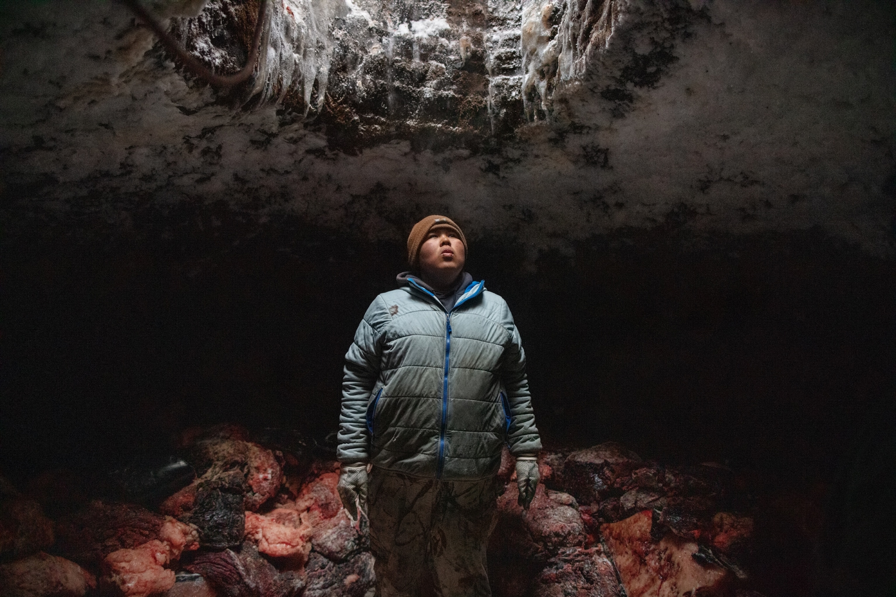 a young man standing on floor covered with meat pieces looking up into cave entrance.