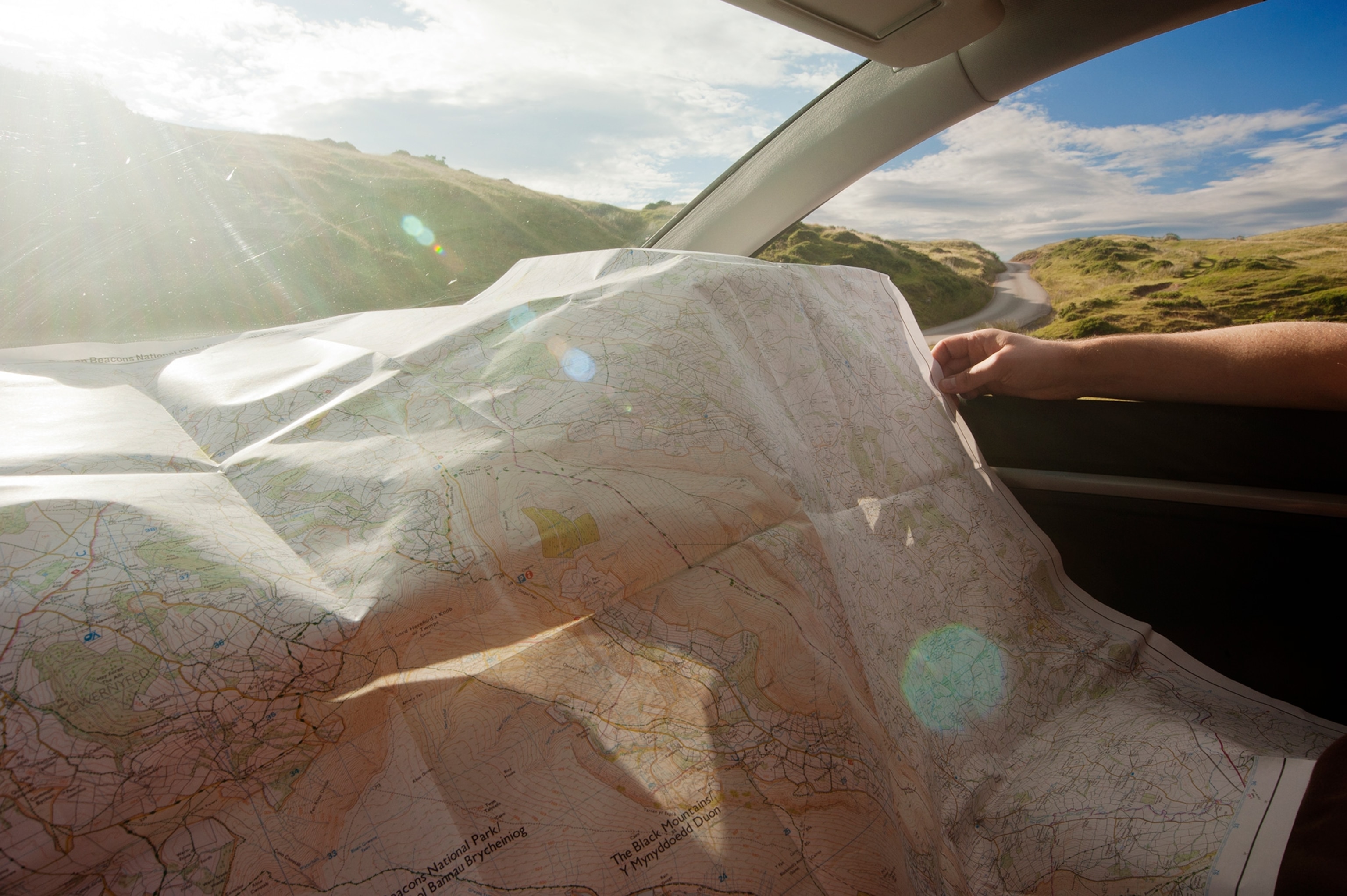 A detailed map is being scrutinised in bright sunshine, over the dashboard of a parked car, as the driver considers which direction to head over the highest road in Wales.