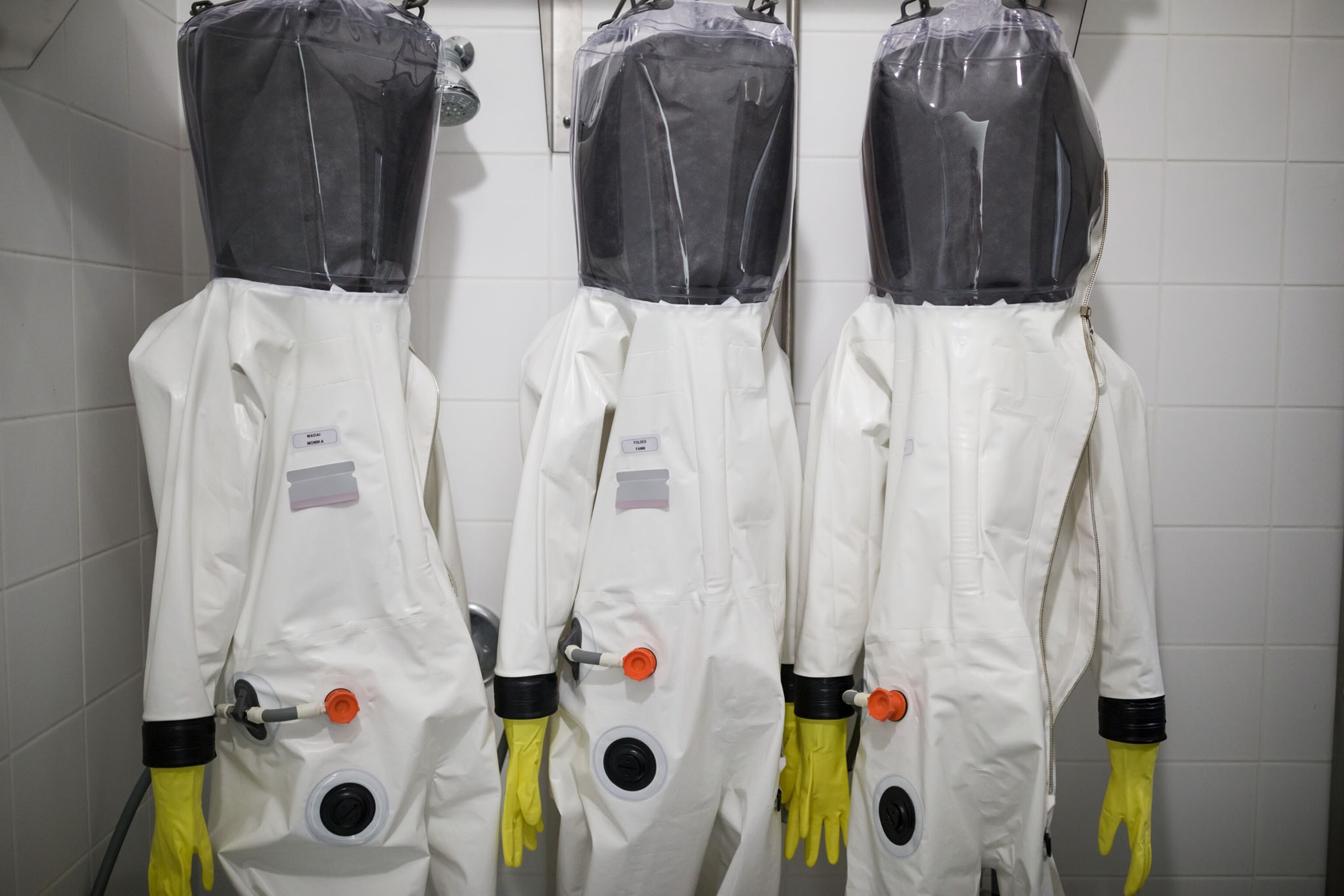 three persons in white protective suits with black face shields.